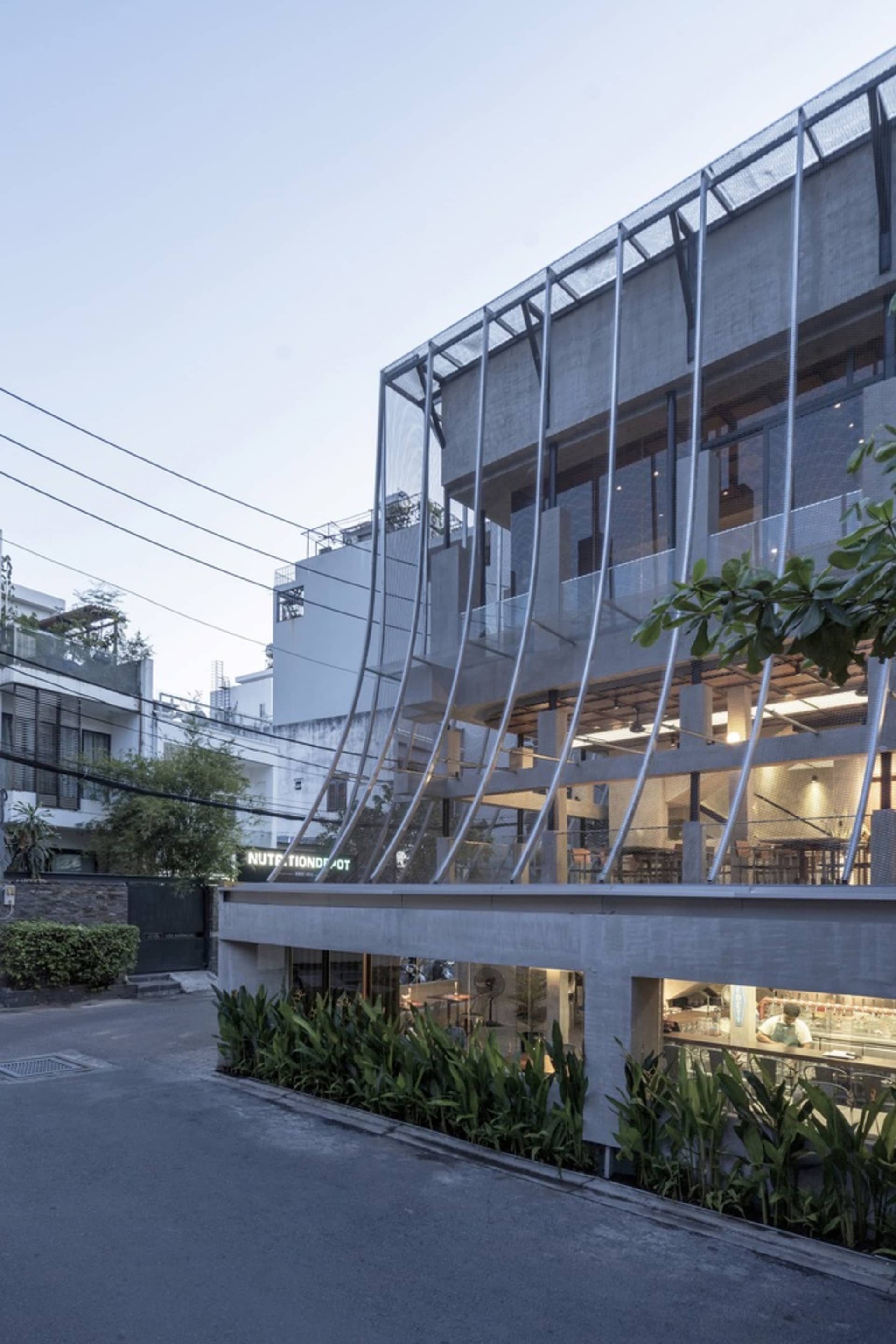 A modern building with a large glass storefront, surrounded by potted plants and natural light