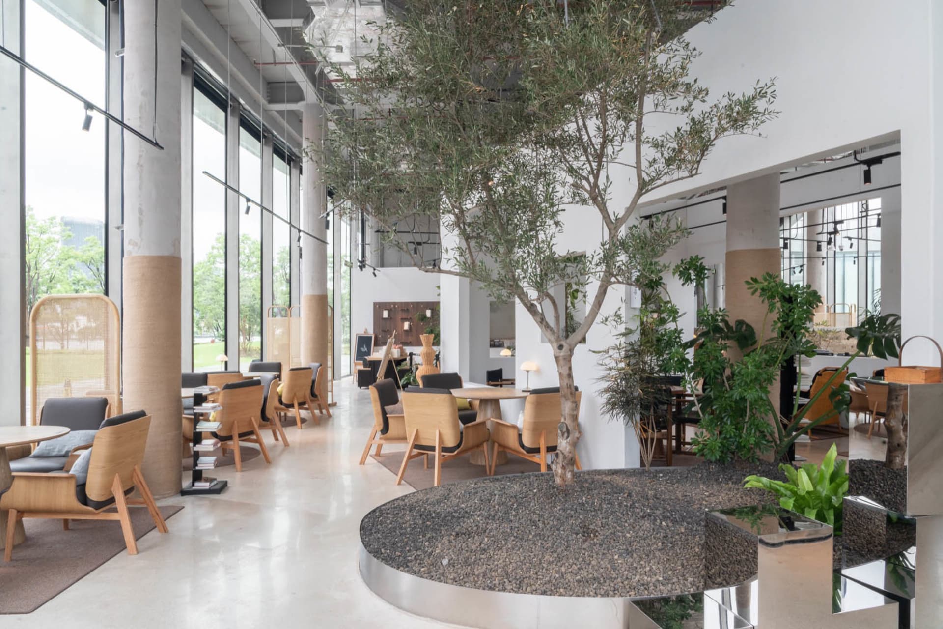開放式現代客廳區域，配有圓形餐桌、盆栽植物、白色牆面，以及木質與金屬家具的混搭，窗戶灑入自然光線