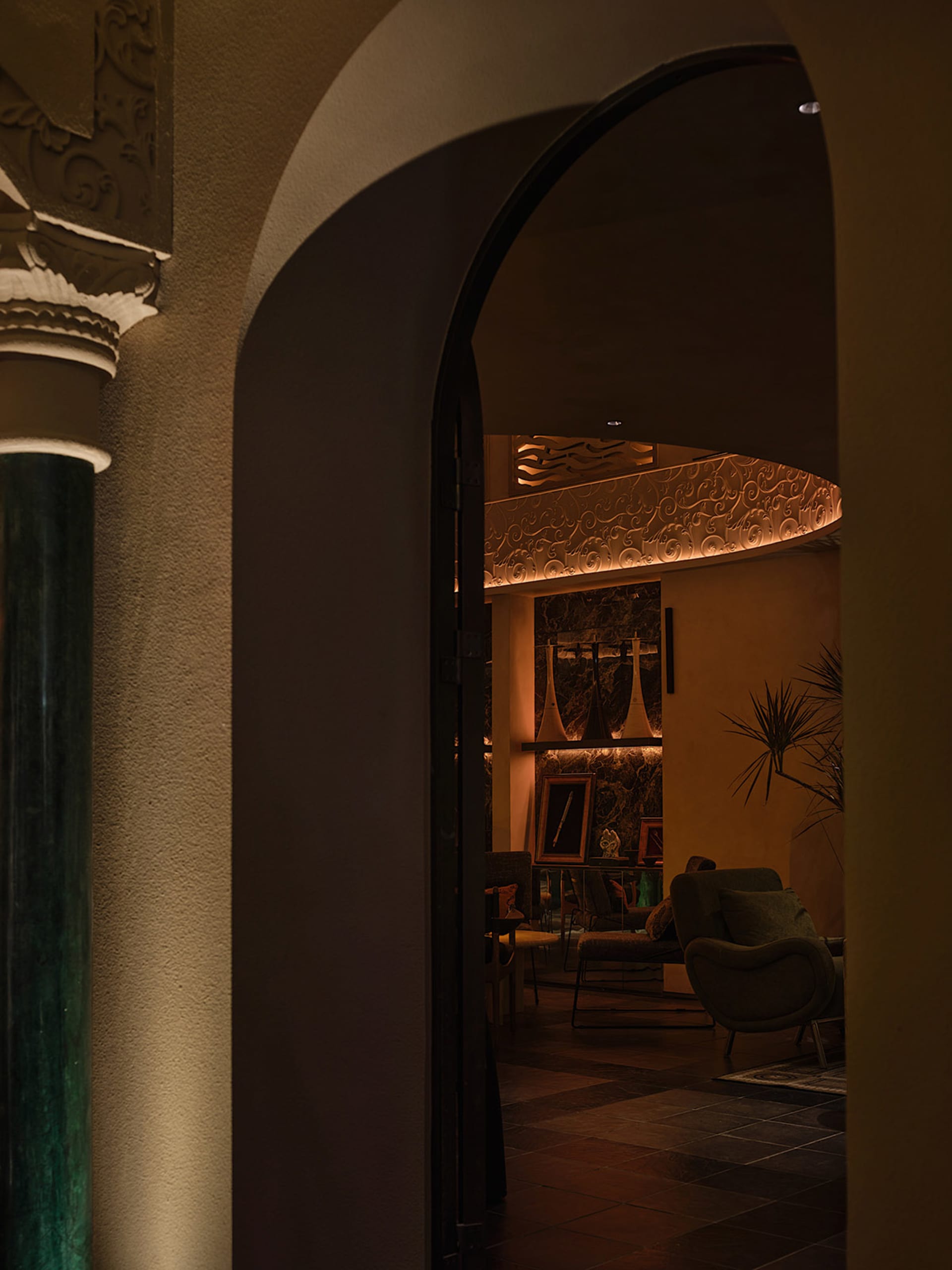 Cozy living space with an archway, two chairs, a potted plant, and a sense of depth and connection to another room