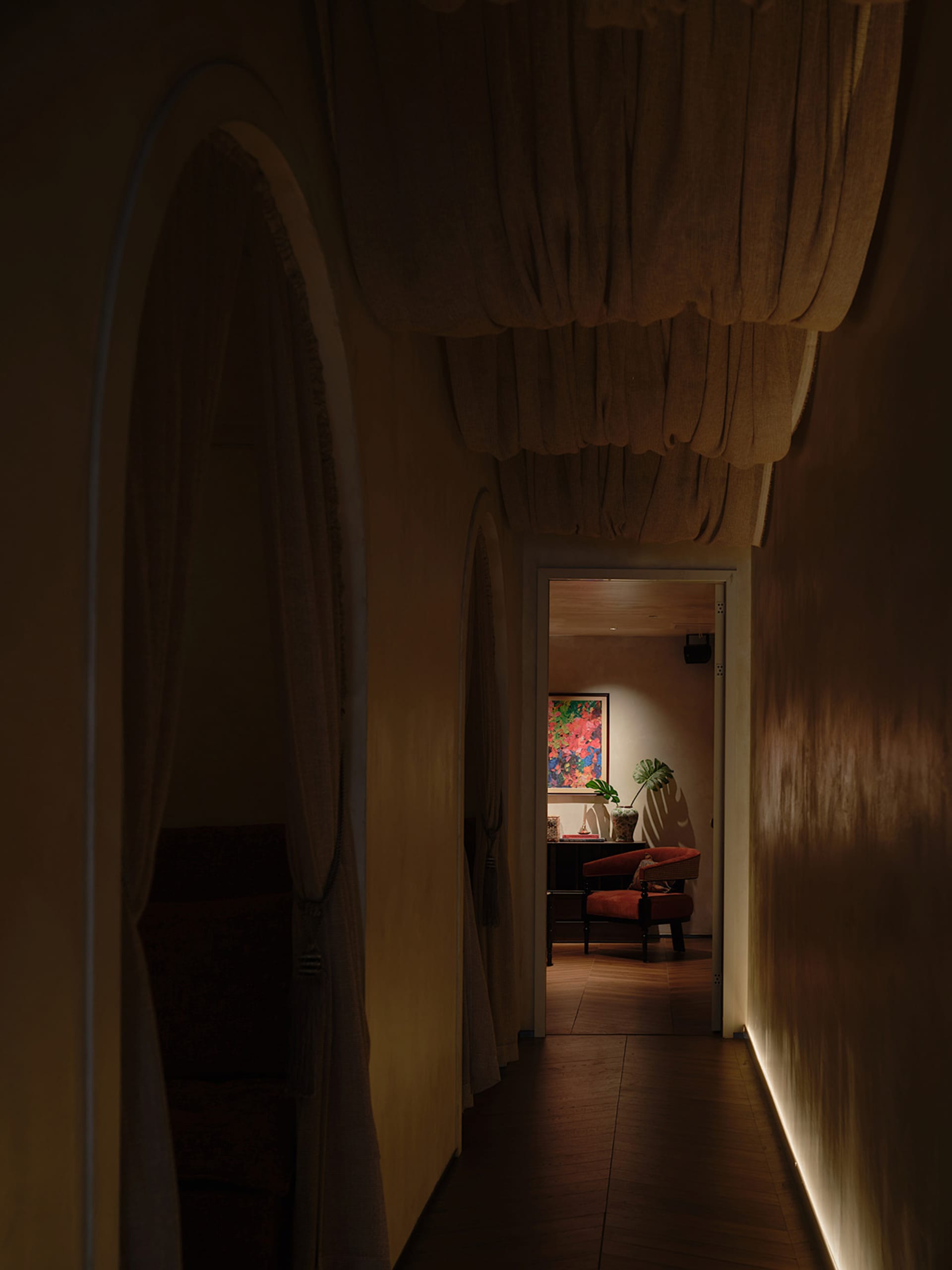 A dimly lit hallway with a yellow wall, two chairs, and a potted plant, creating a cozy atmosphere