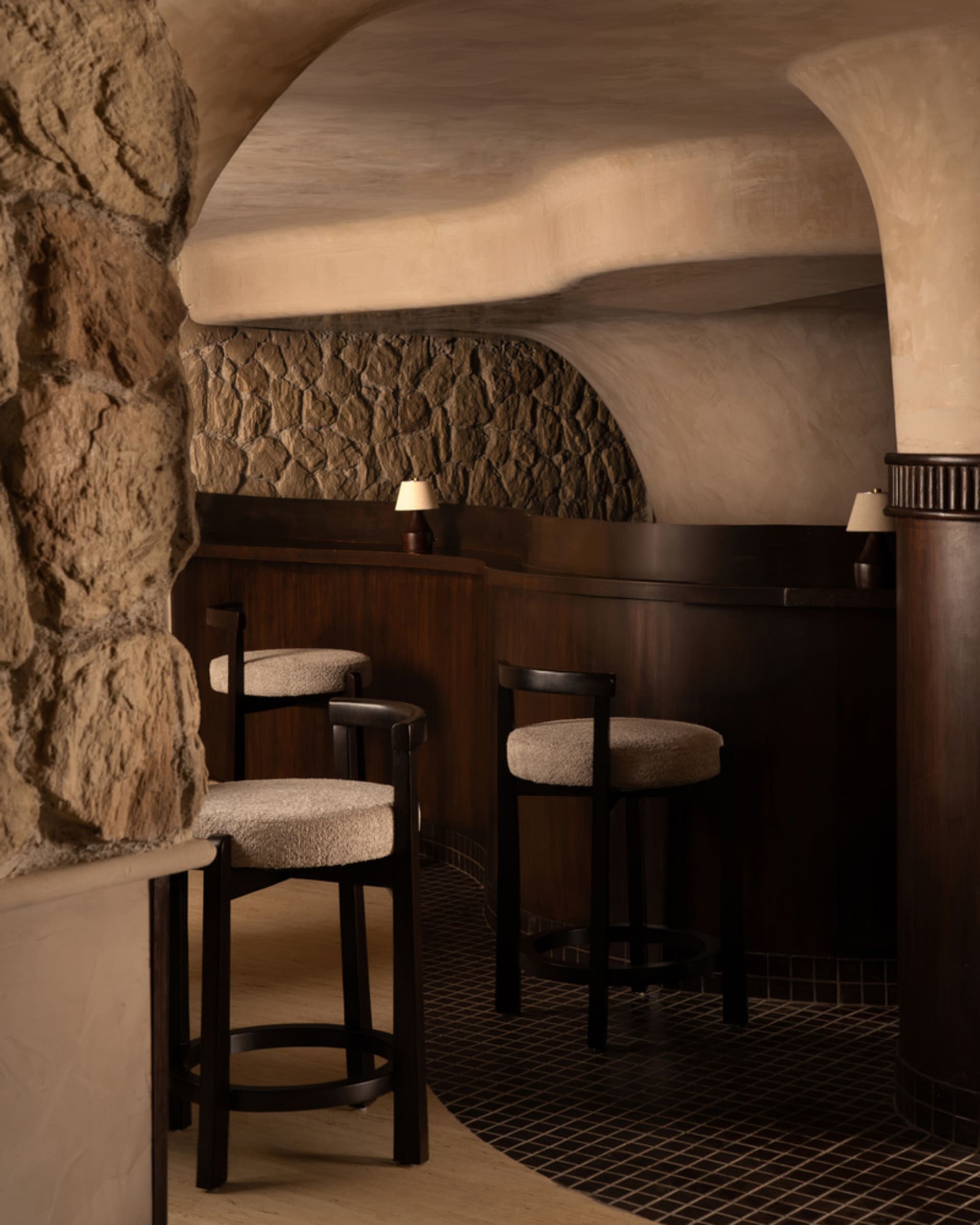 Cozy bar area with a stone wall, wooden floors, and a brown bar counter, lit by two lamps
