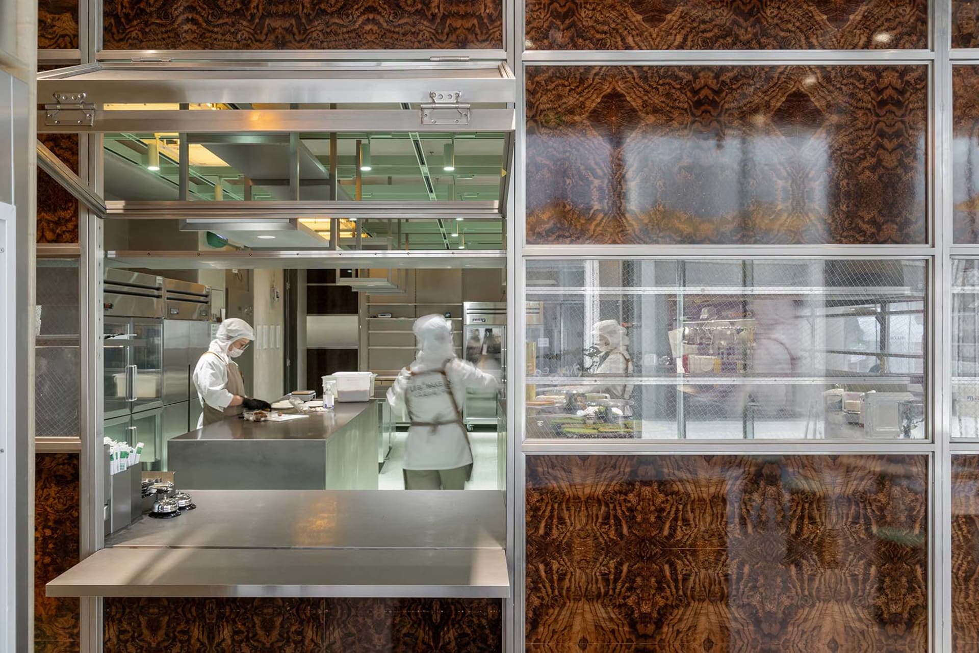 Industrial kitchen with two ovens, a sink, and three people in white uniforms preparing food in a professional and organized workspace