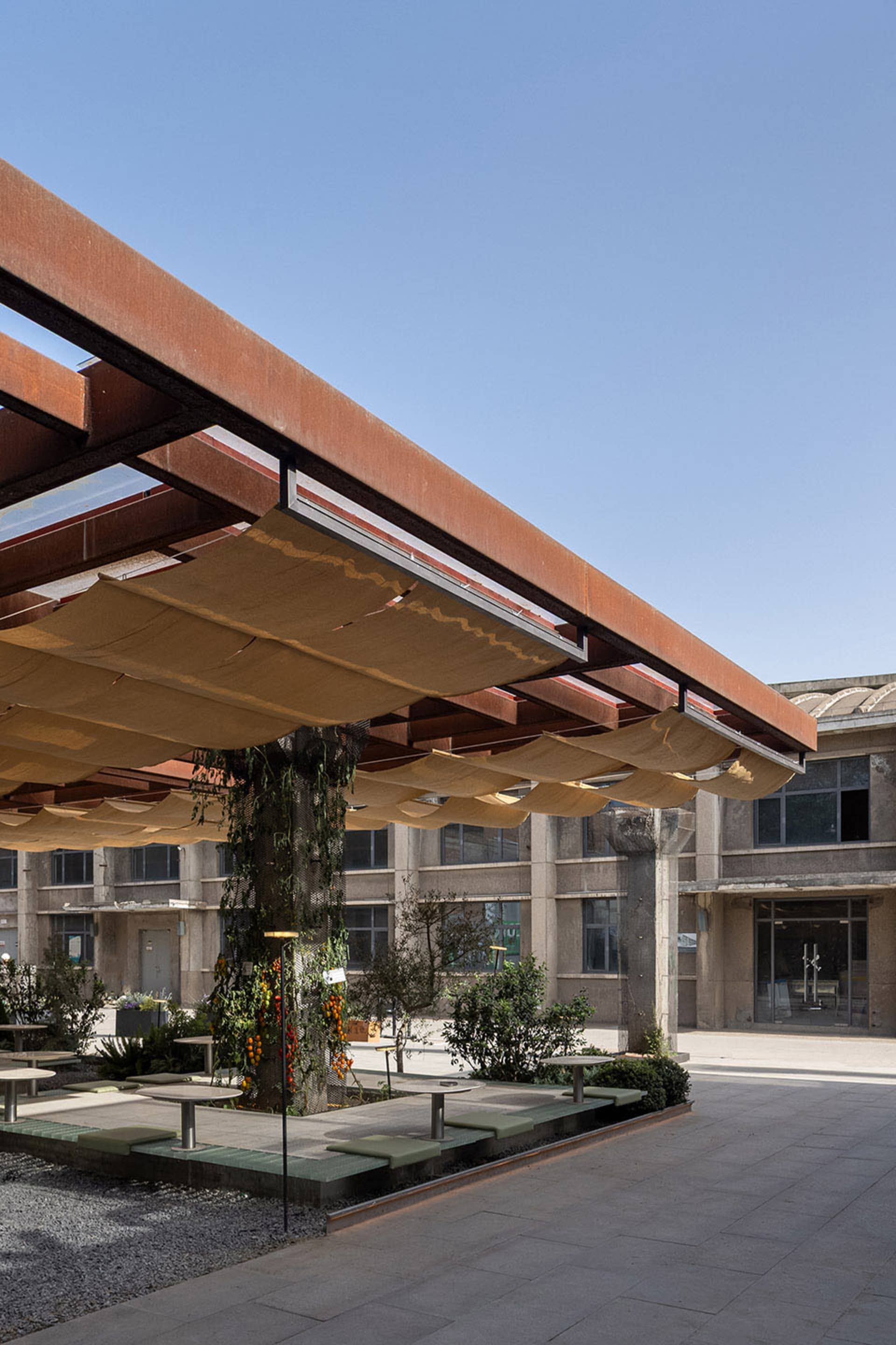 A modern plaza with a metal roof, multiple windows, benches, and potted plants, conveying urban design and functionality