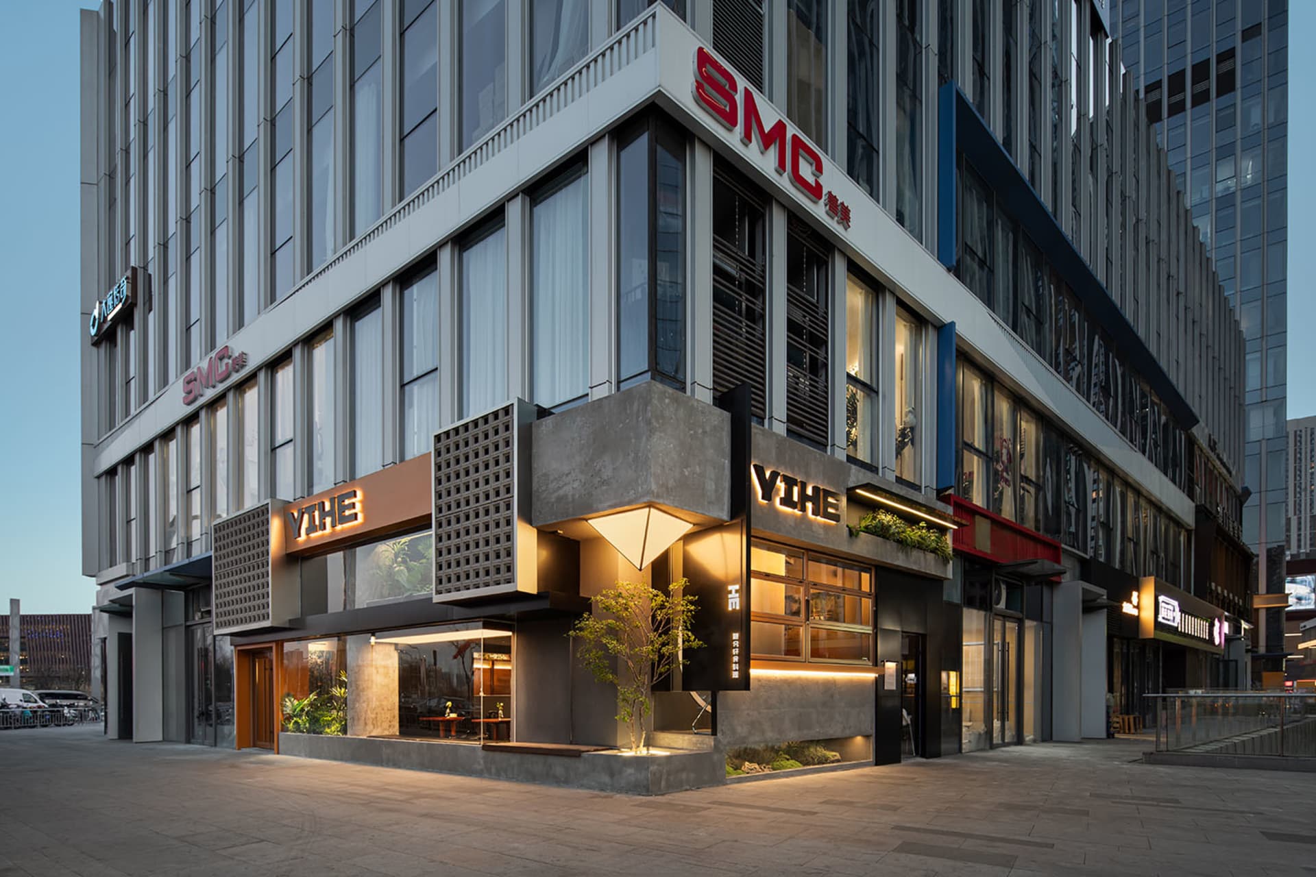 熱鬧的都市街景，展示一座擁有石材與玻璃立面、巨大招牌及前方樹木的商業大樓