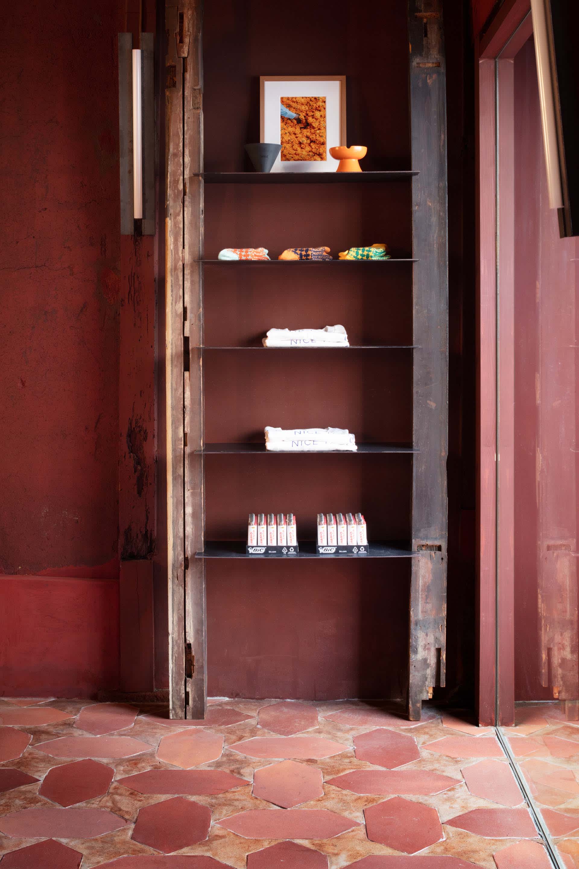 A wooden bookshelf in a cozy room with red walls, holding books, towels, and other items, conveying a sense of comfort and functionality