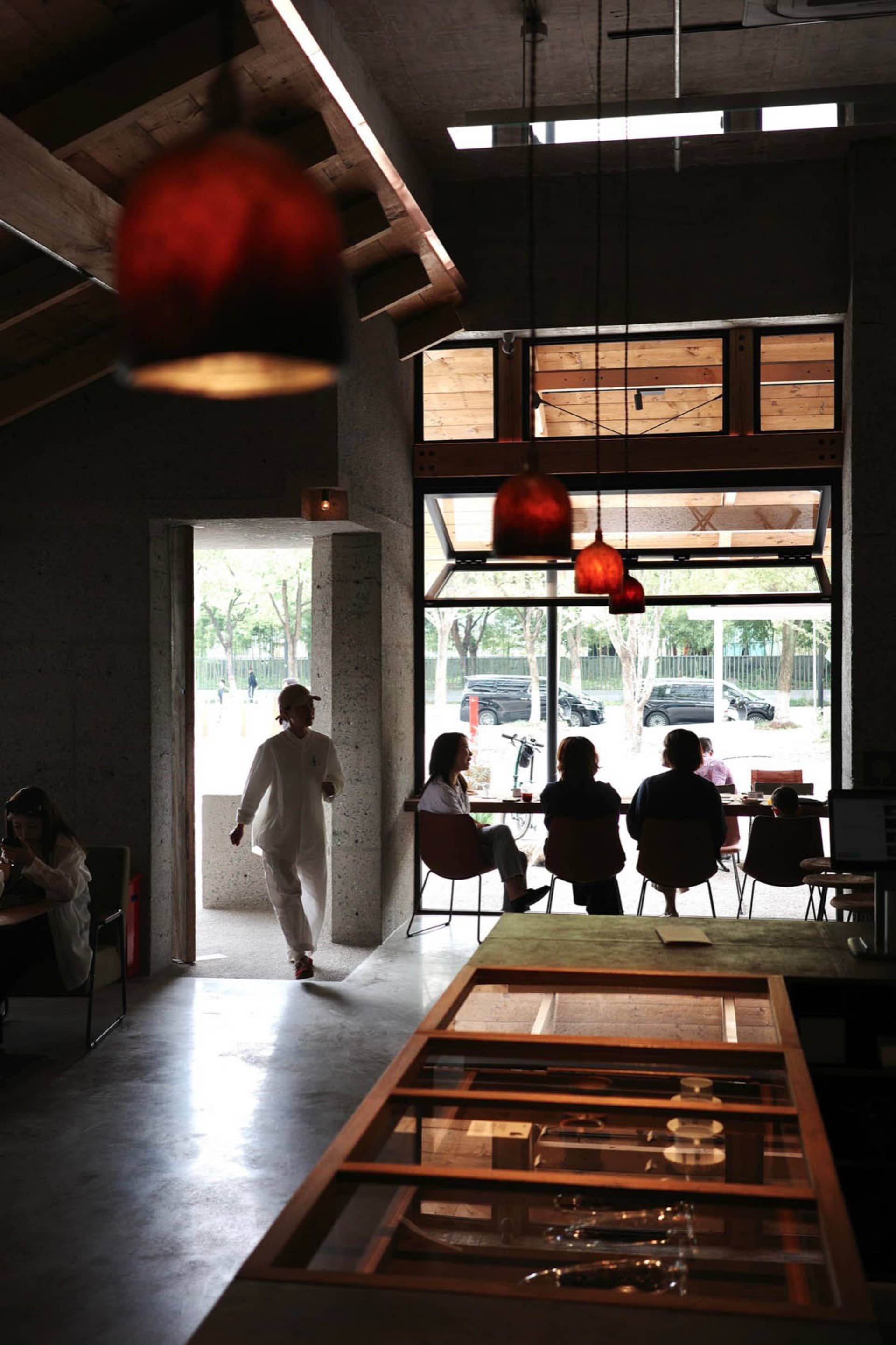 A casual indoor space with concrete walls, dining tables, chairs, and bicycles, featuring people enjoying a relaxed atmosphere