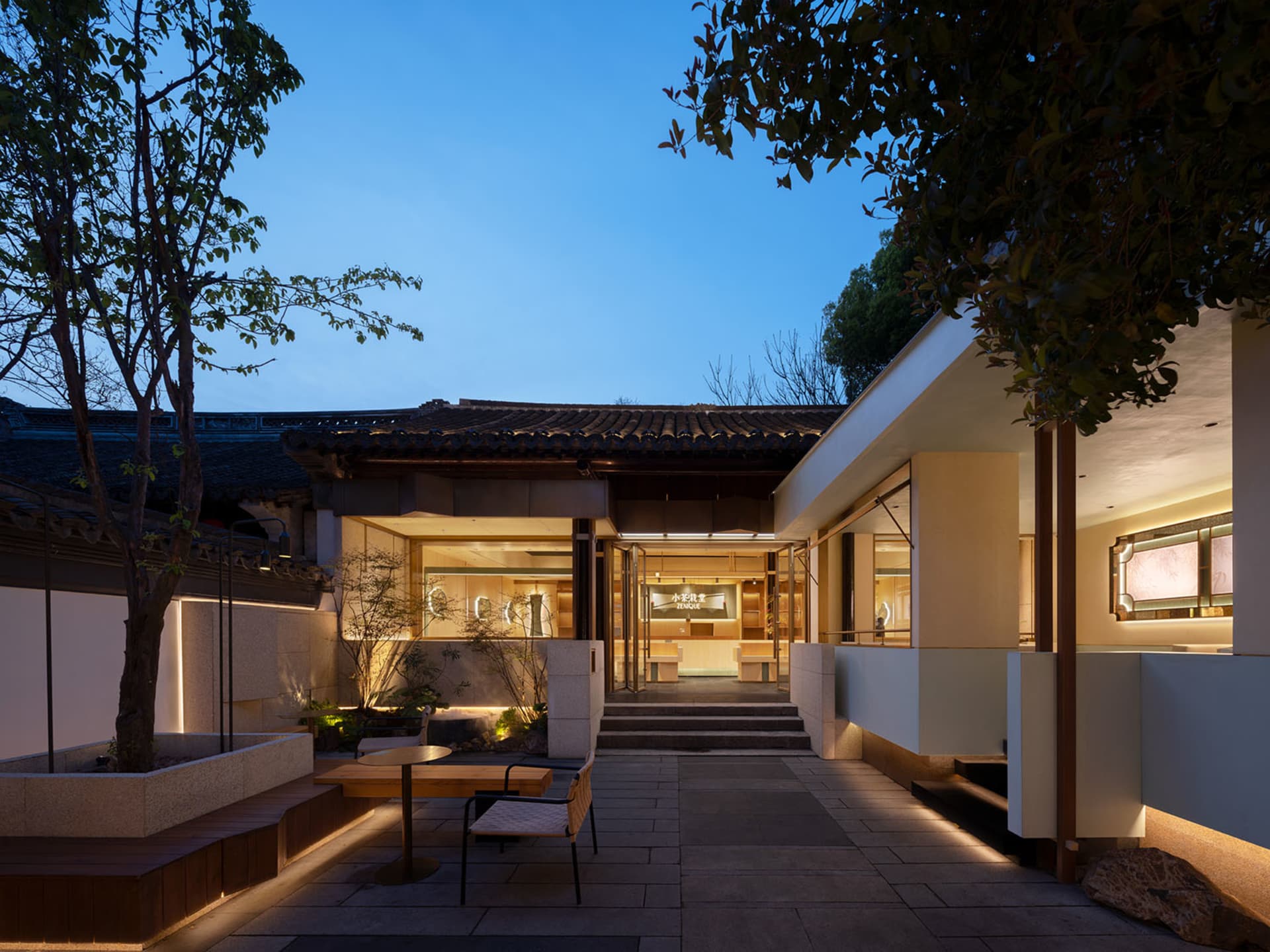 Asian-style building with a wooden exterior, large glass window, patio area, and potted plants
