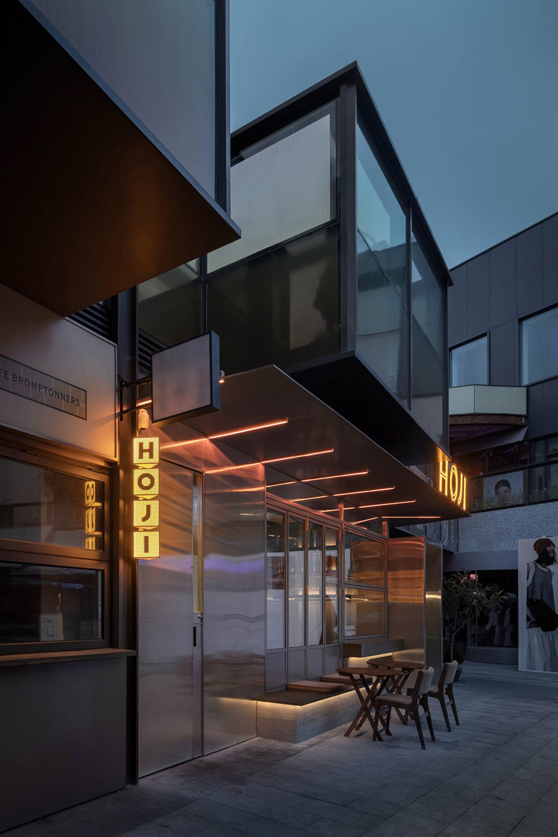 A modern building exterior at night with a large glass front, various window sizes and shapes, and artificial lighting creating a warm glow