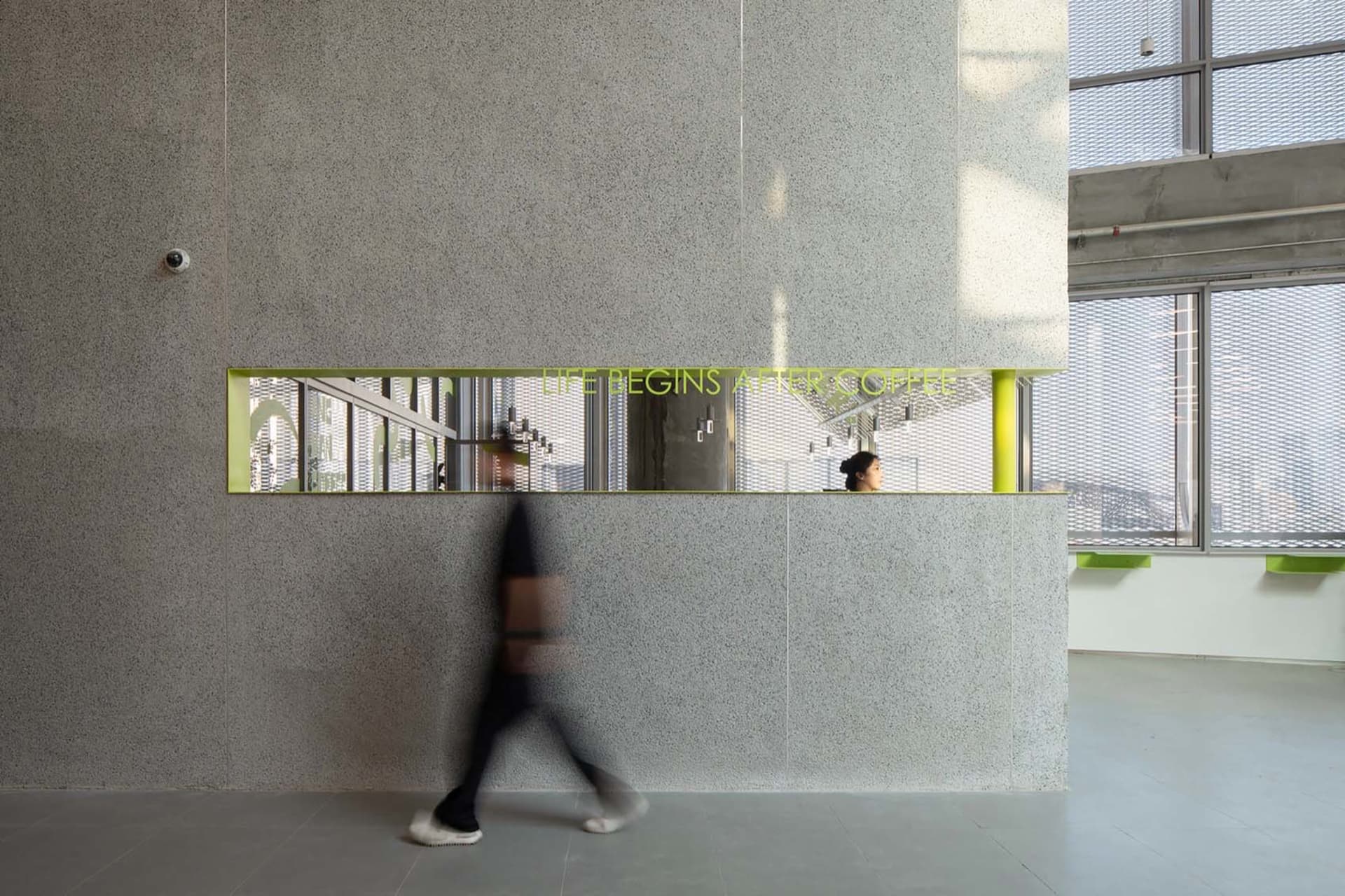 A man walks down a professional office hallway with two other people present, surrounded by a focused work environment