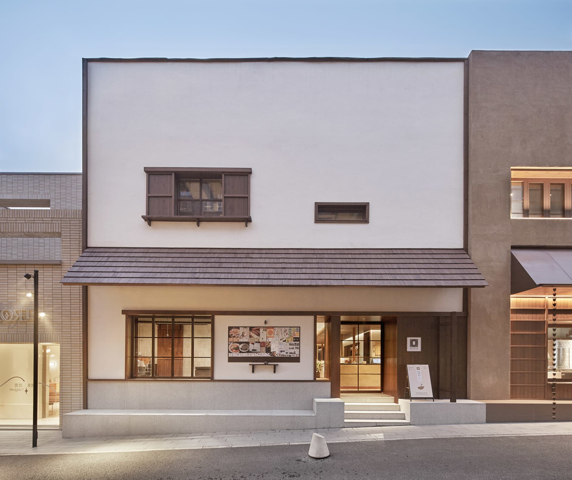 A modern building with a white exterior, brown roof, and wooden door, featuring a clock on the wall and two chairs in the scene