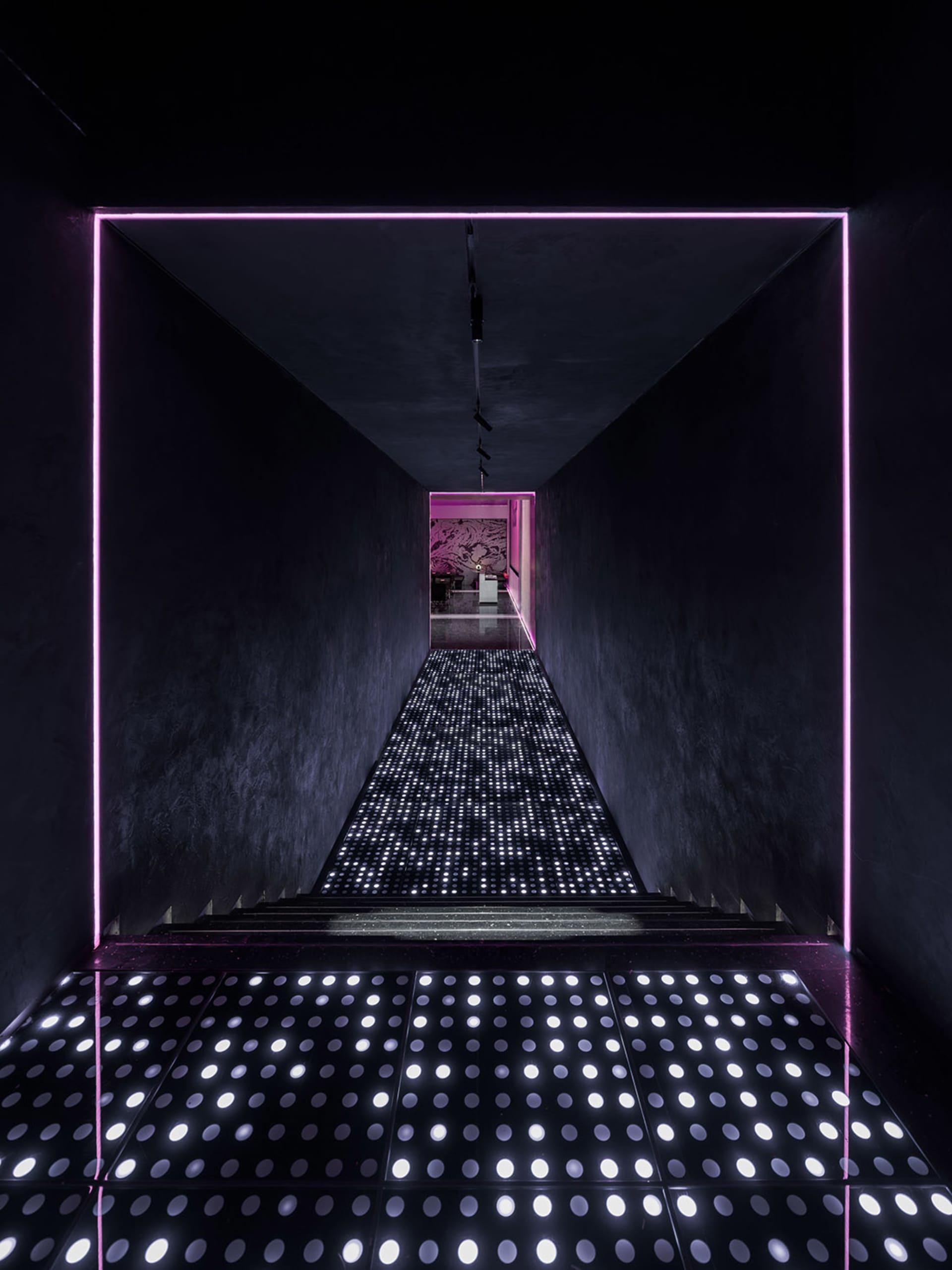 A dark and sleek hallway with a black background, illuminated pathway, and contemporary design elements