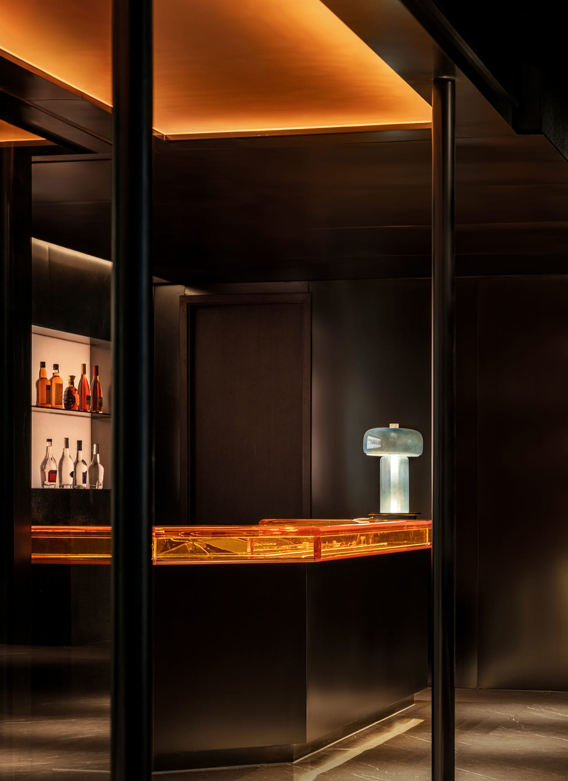 A dark bar area with a countertop featuring various bottles of liquor, creating a cozy and intimate atmosphere for patrons to enjoy their drinks