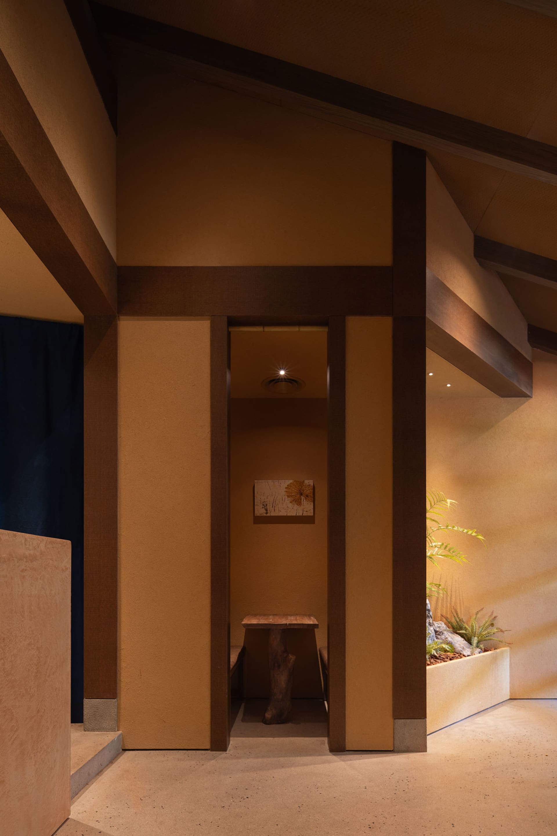 A small room with a brown color scheme, featuring a wooden doorway, two potted plants, and a bench for seating