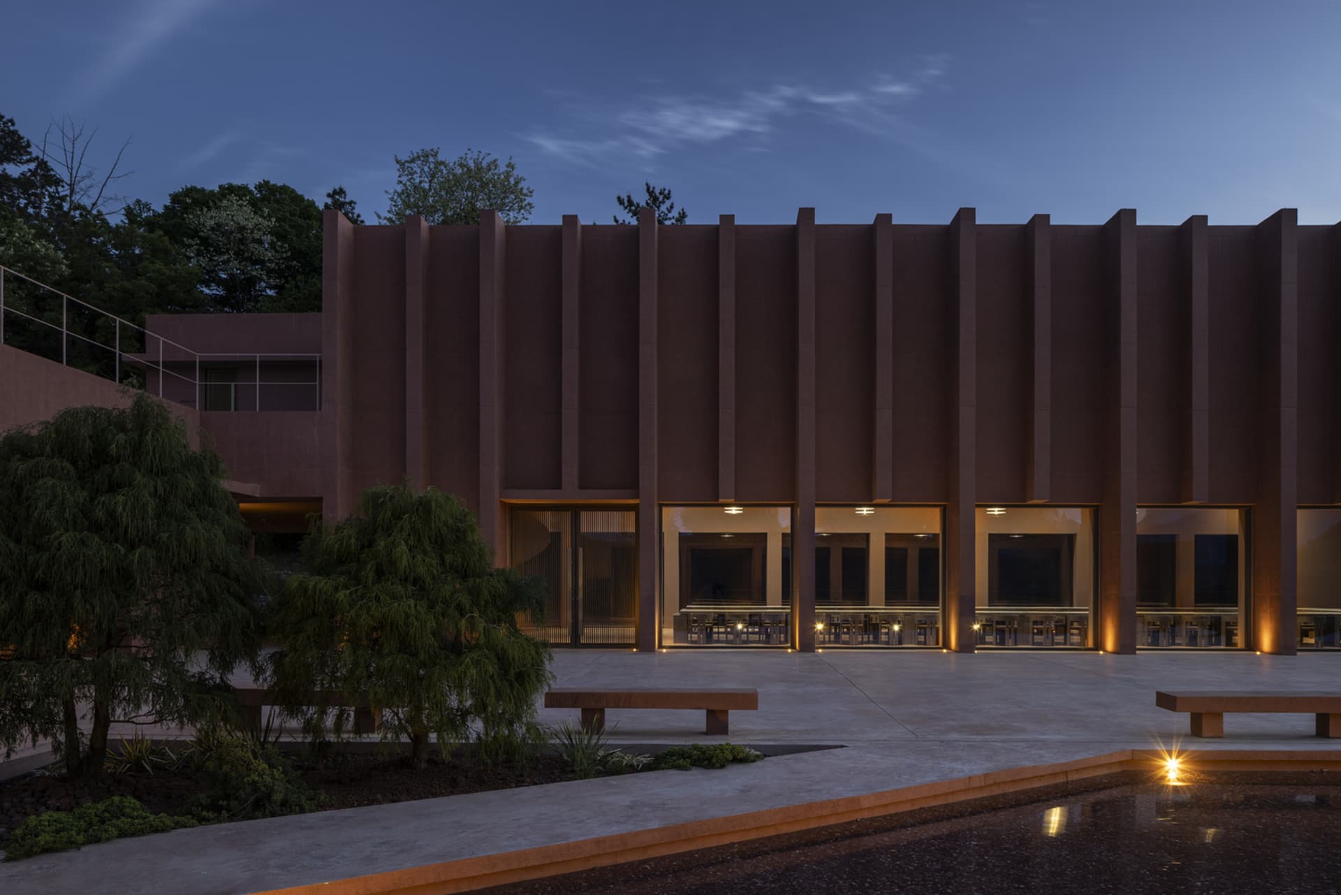 A brown building with multiple windows in various shapes and sizes, surrounded by outdoor benches