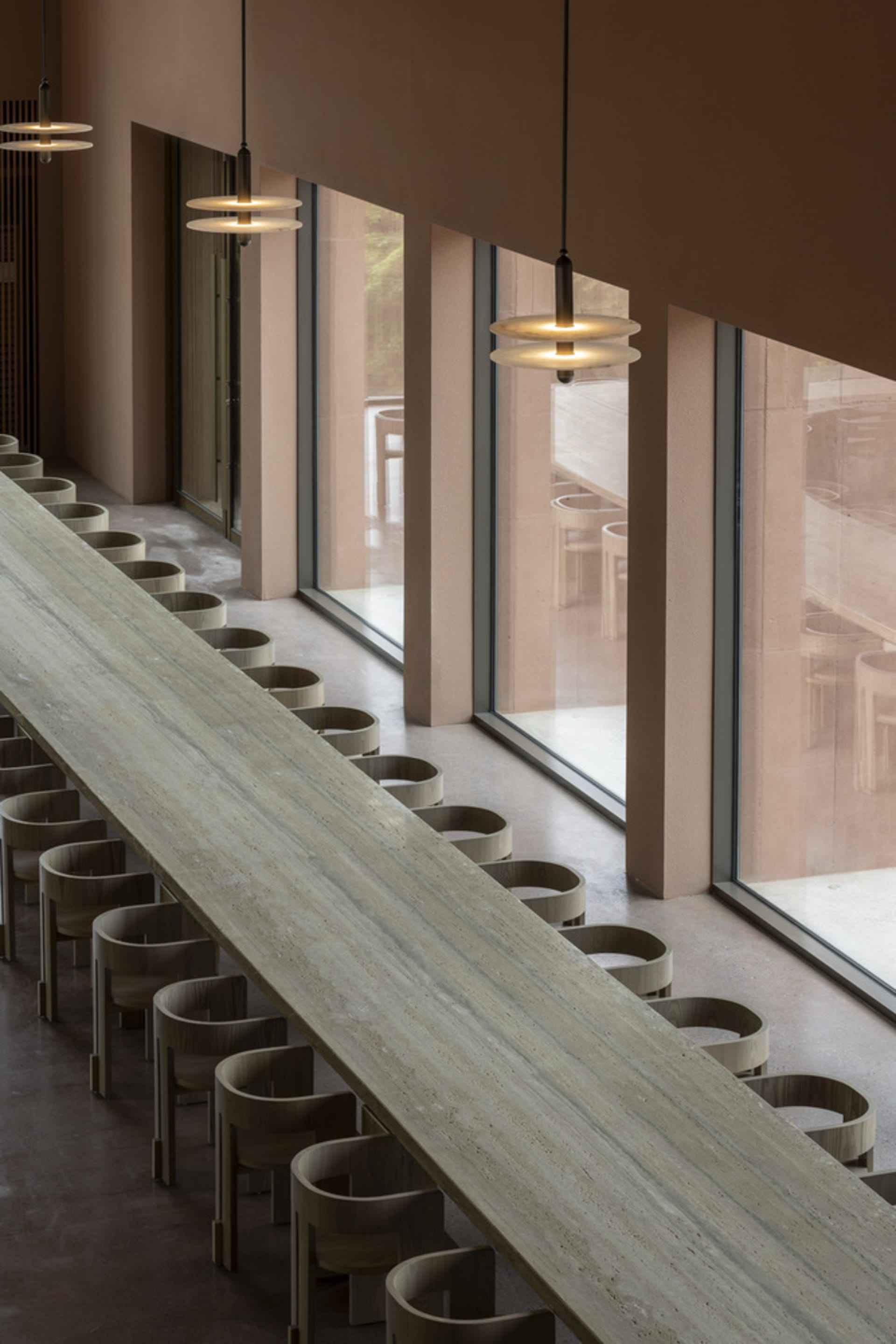 A well-lit restaurant with a long dining table, chairs, and natural light from windows