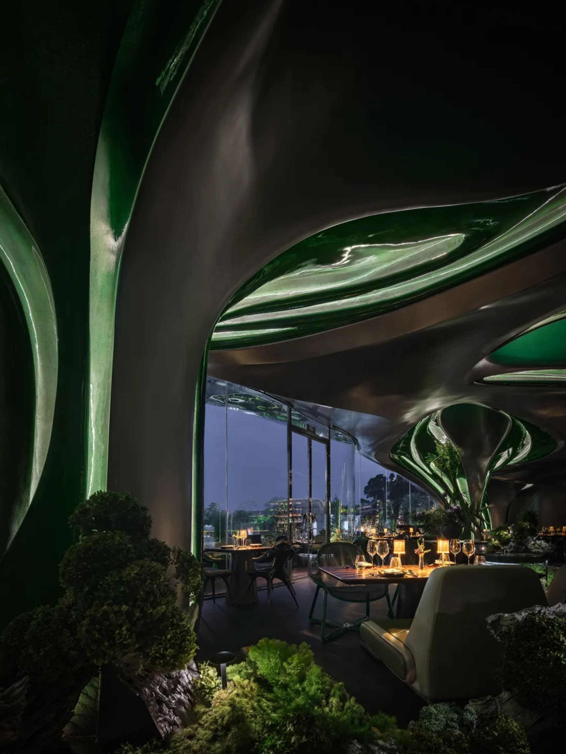 A cozy restaurant dining area with a large green wall, multiple chairs, and dining tables with wine glasses and bottles