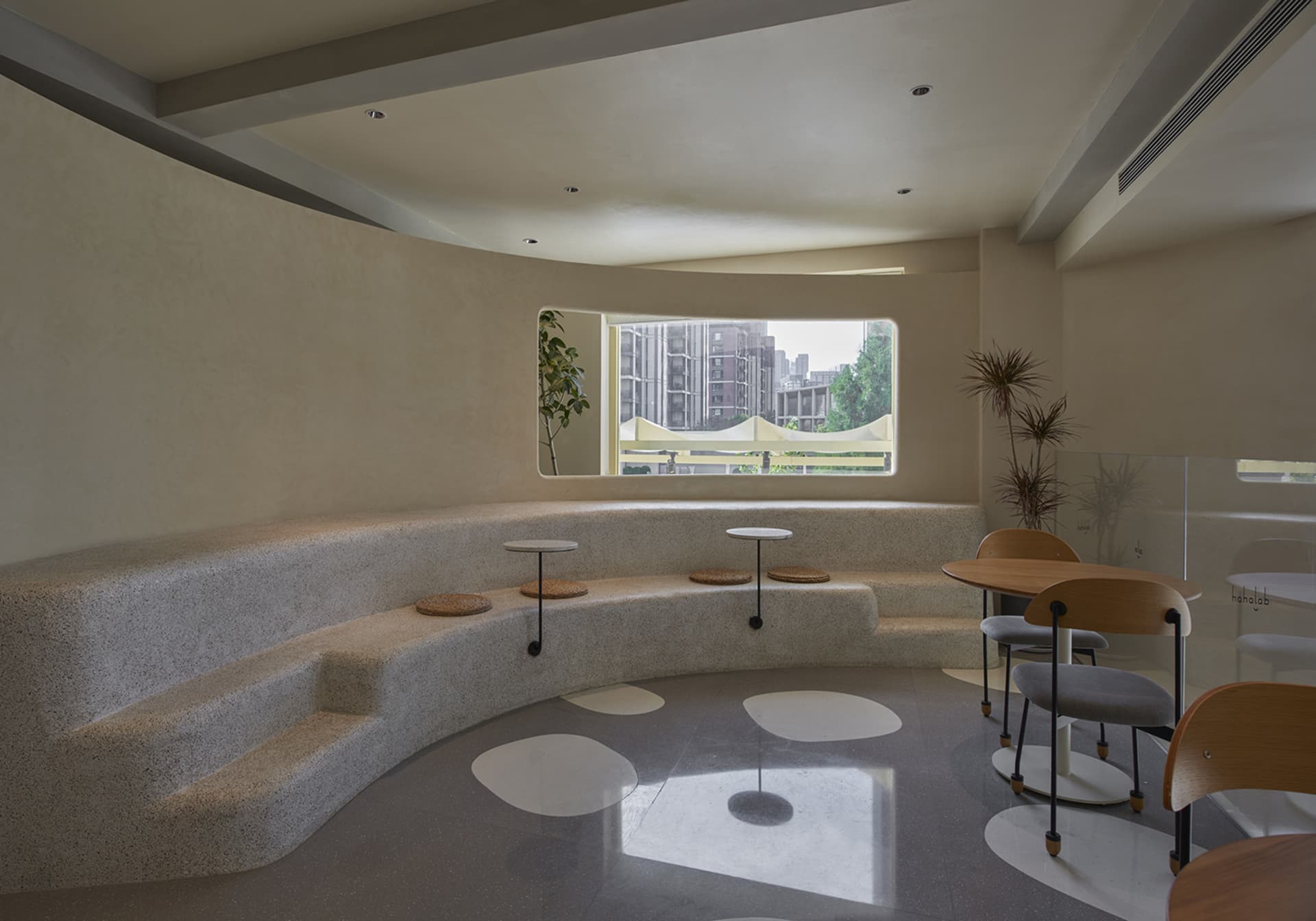 A well-lit room with a curved bench and chairs, three round tables, and a window, creating a comfortable and inviting atmosphere for socializing or dining