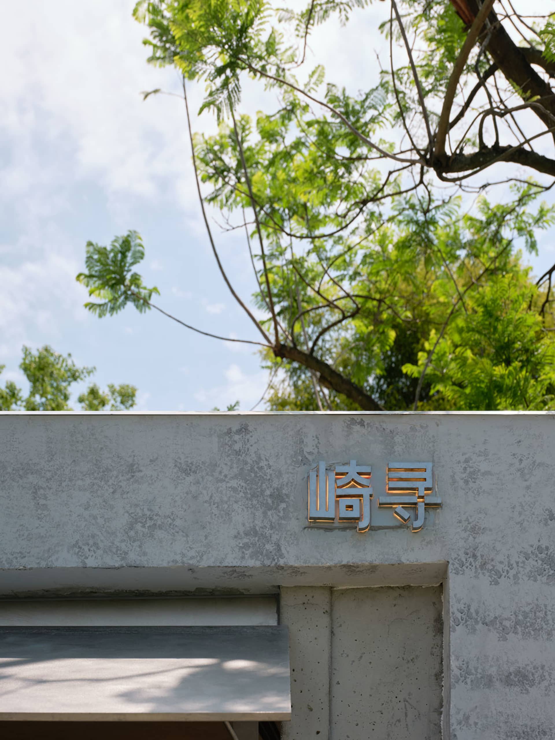 灰色混凝土建築，帶有金屬招牌與現代外觀，周圍環繞樹木，位於都市環境中