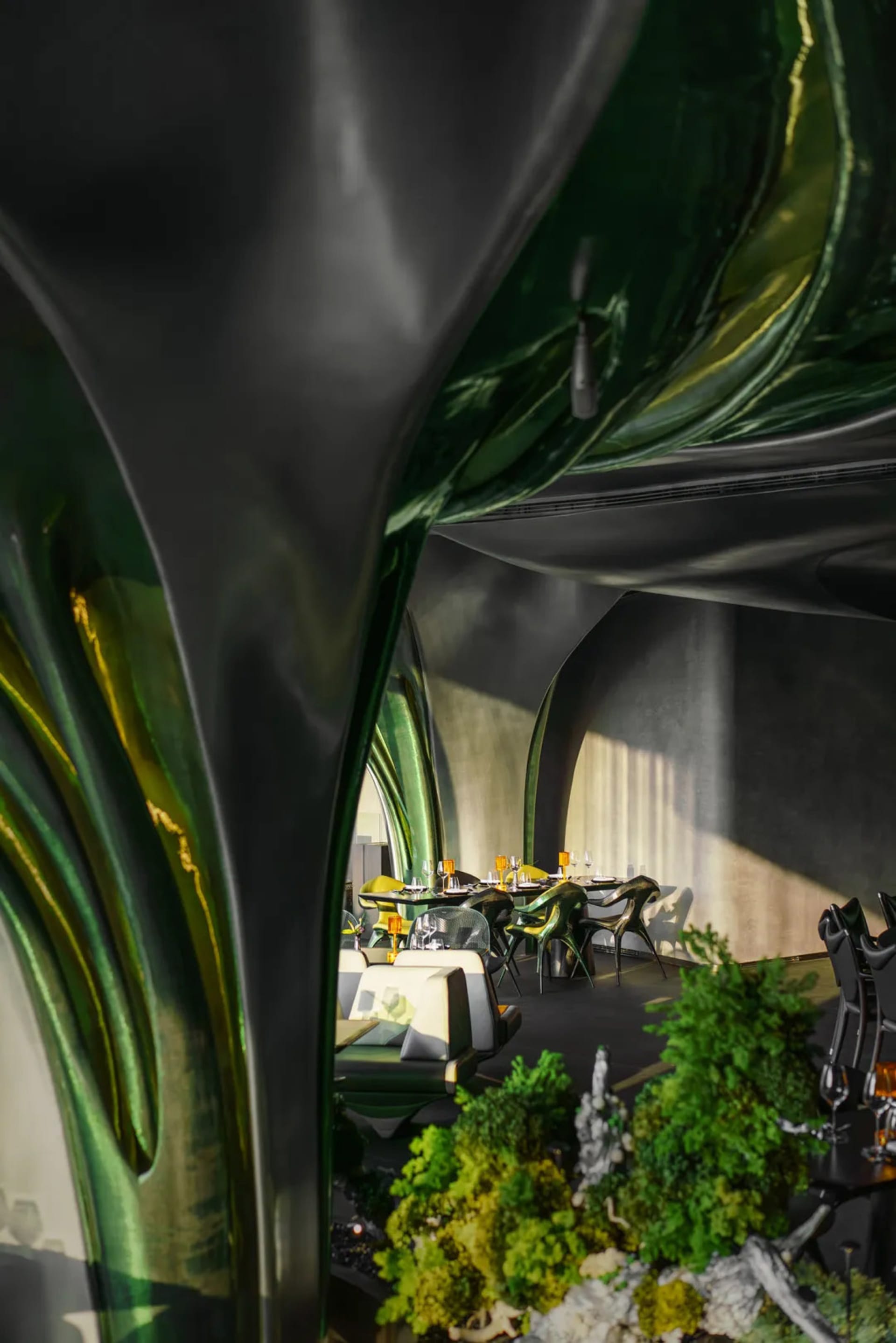 Casual restaurant dining area with multiple tables, chairs, and potted plants, with backpacks on some chairs