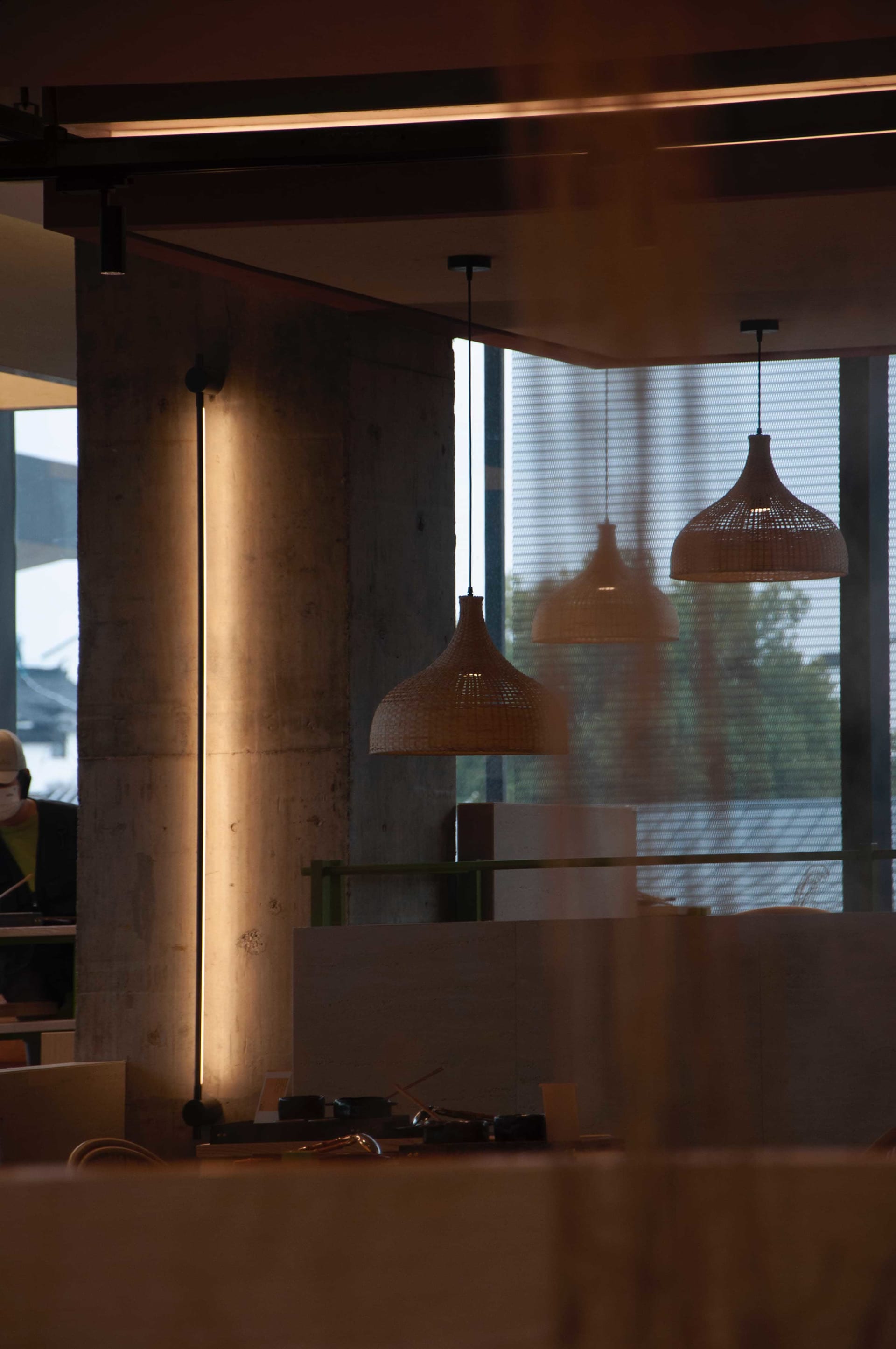 Interior view of a modern office space with concrete walls, wooden elements, and hanging lamps providing illumination
