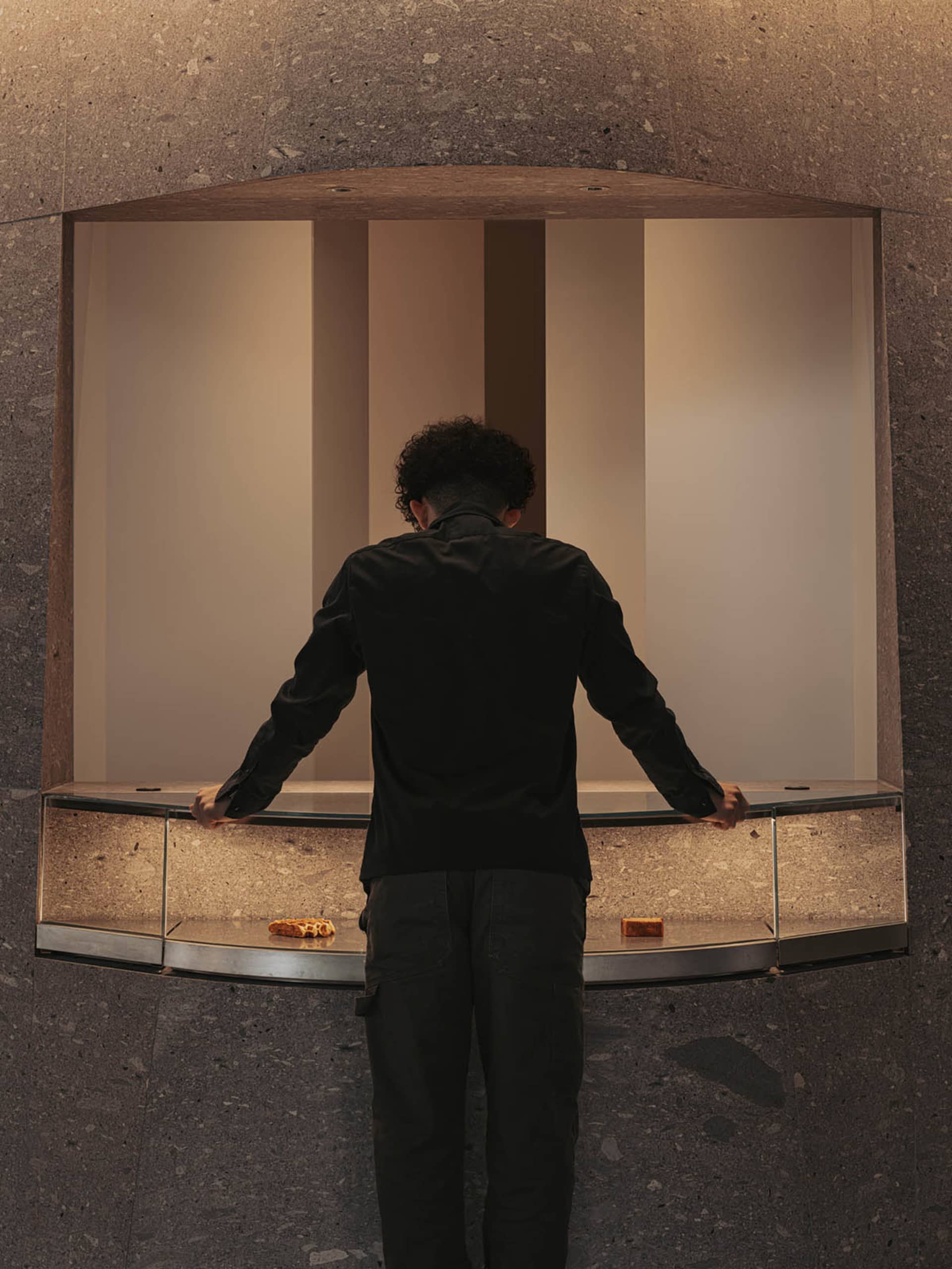A man stands at a counter in a casual restaurant, looking down at something on the counter, in a relaxed atmosphere
