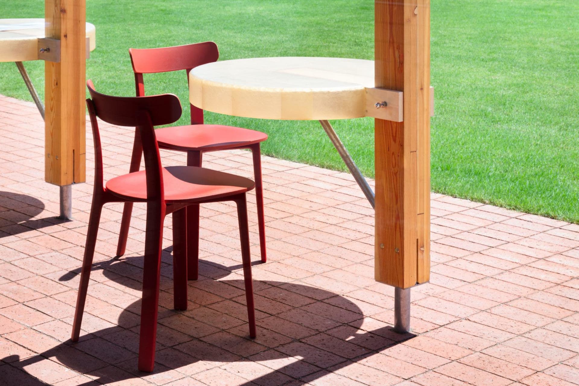 An inviting outdoor patio with two red chairs and two dining tables on a brick surface, perfect for al fresco dining or conversations
