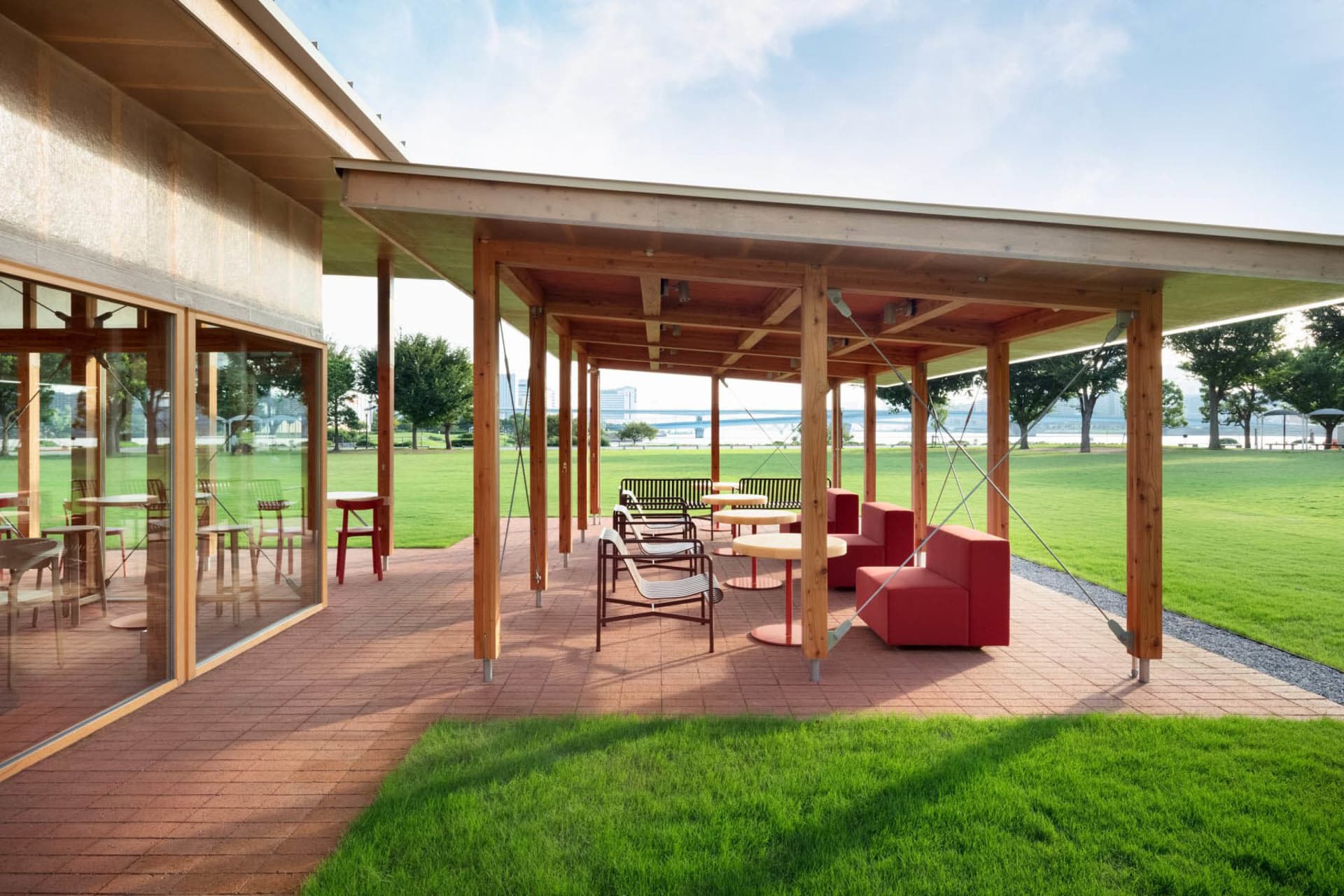An open-air patio with a wooden structure, red roof, and comfortable seating areas for socializing and dining