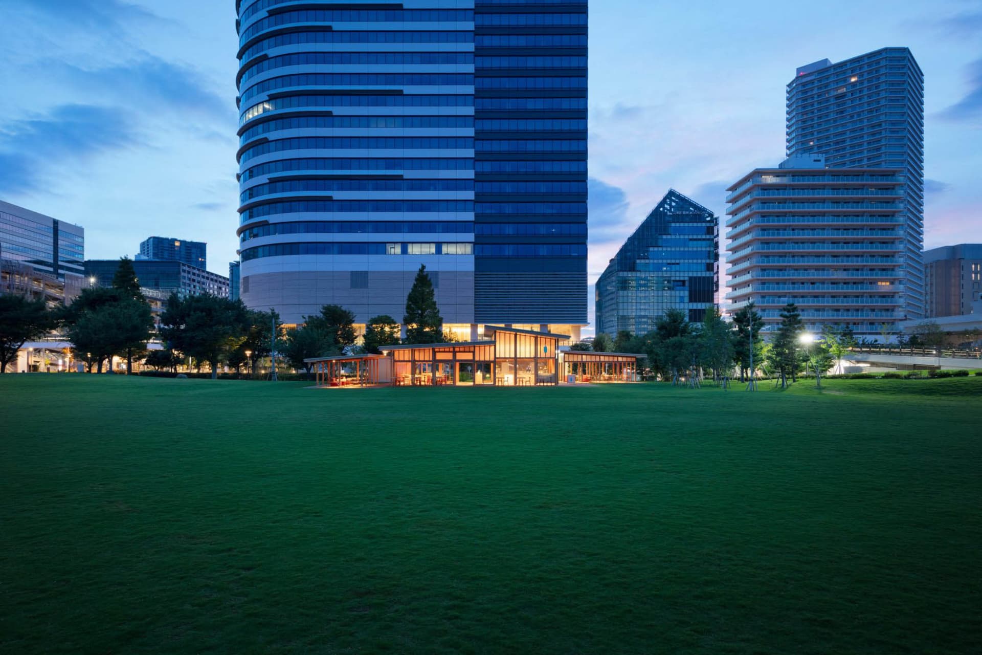 A modern office building with many windows and a striking facade, surrounded by trees in the city at night