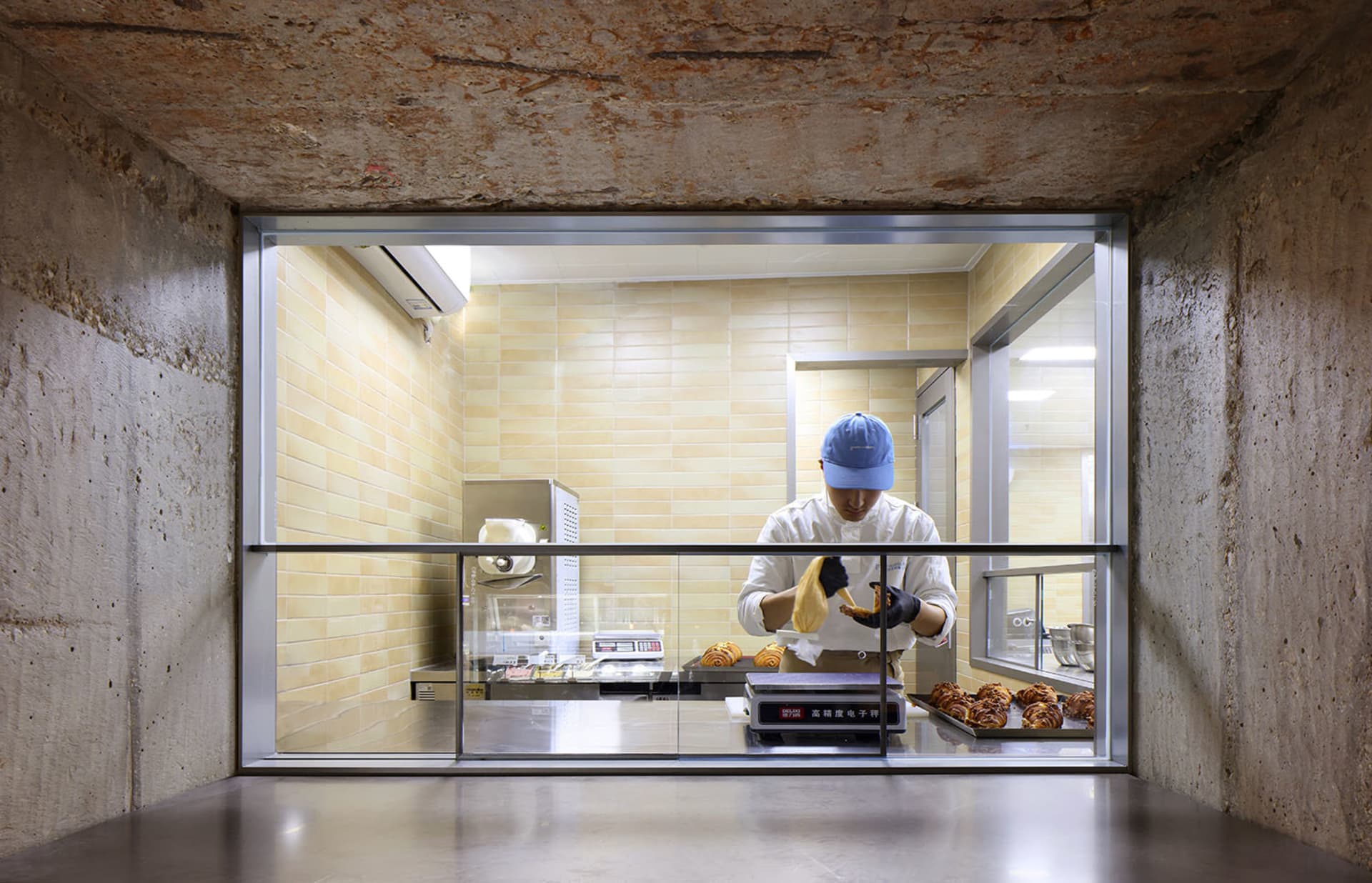 A man in a blue hat prepares food at a counter with multiple donuts and bowls in a professional kitchen environment