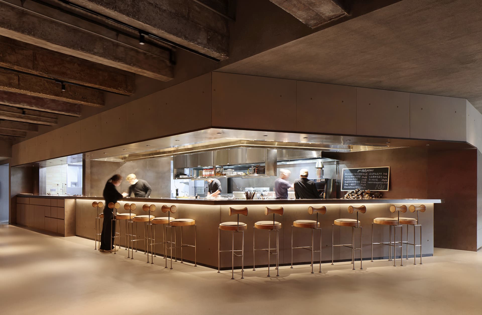 Industrial kitchen with a large countertop, stools, and various cooking and serving items, conveying a functional and efficient atmosphere