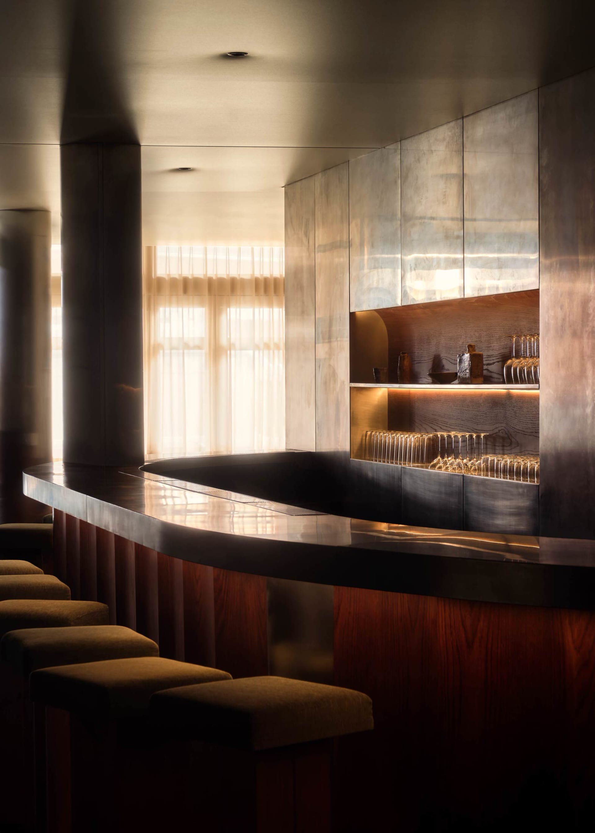 A modern bar area with a large wooden counter featuring a marble top, wine glasses, and bottles, set in a sophisticated and inviting atmosphere