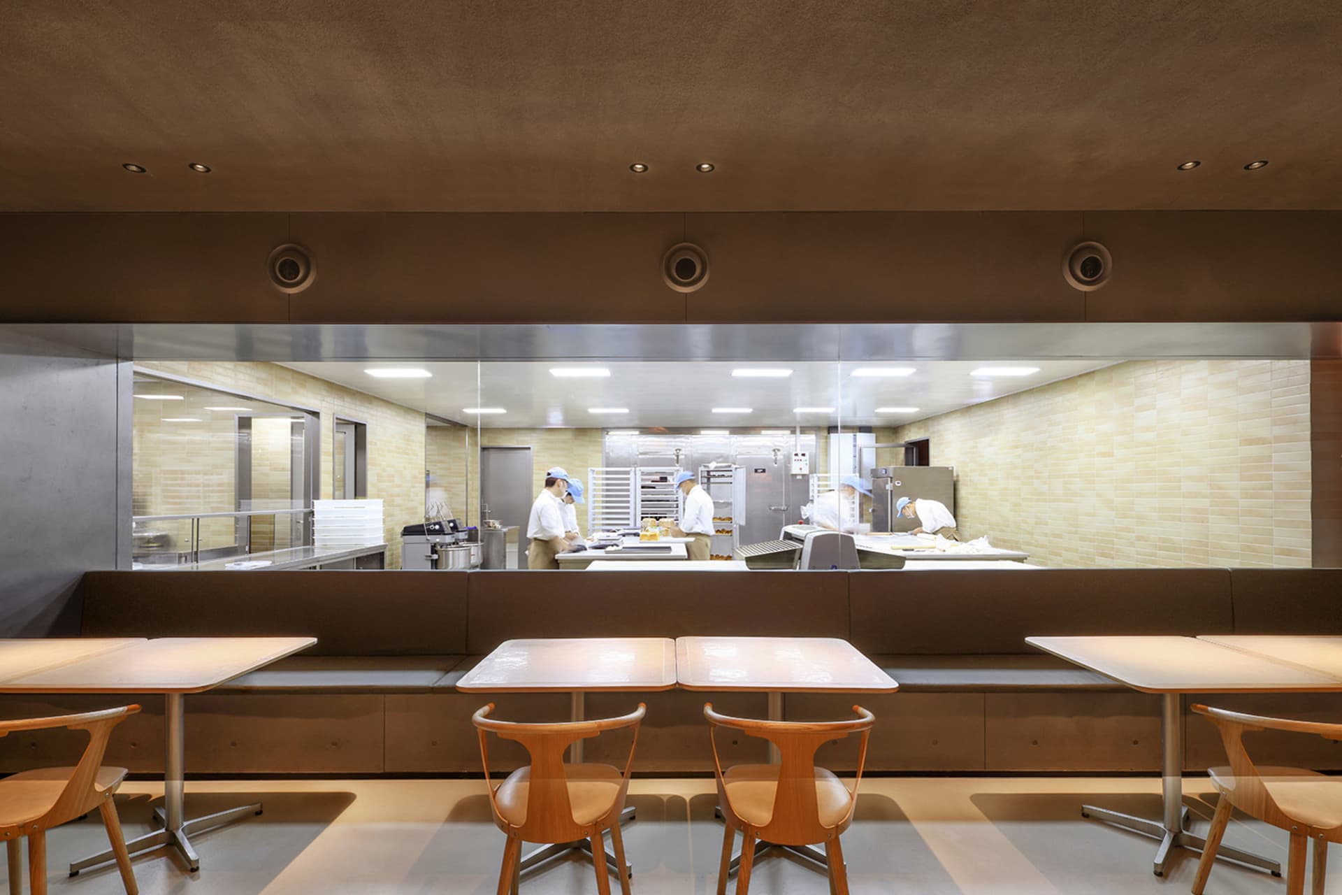 Industrial kitchen dining area with wooden tables, chairs, appliances, and natural light from a window