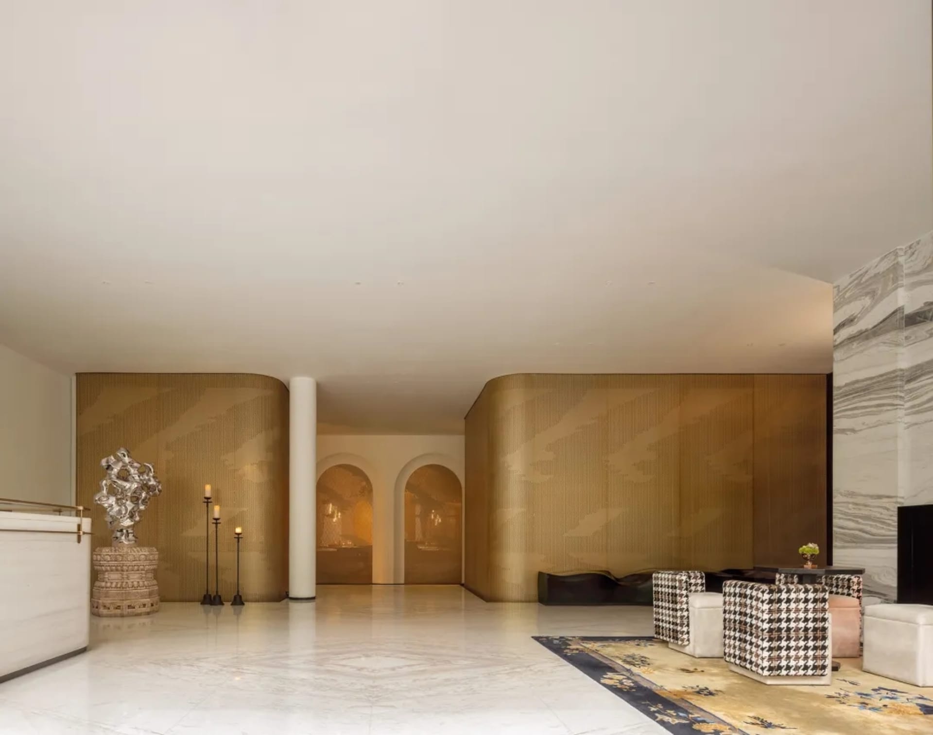 Spacious hotel lobby with a checkered rug, gold accents, two couches, chairs, a dining table, and decorative vases