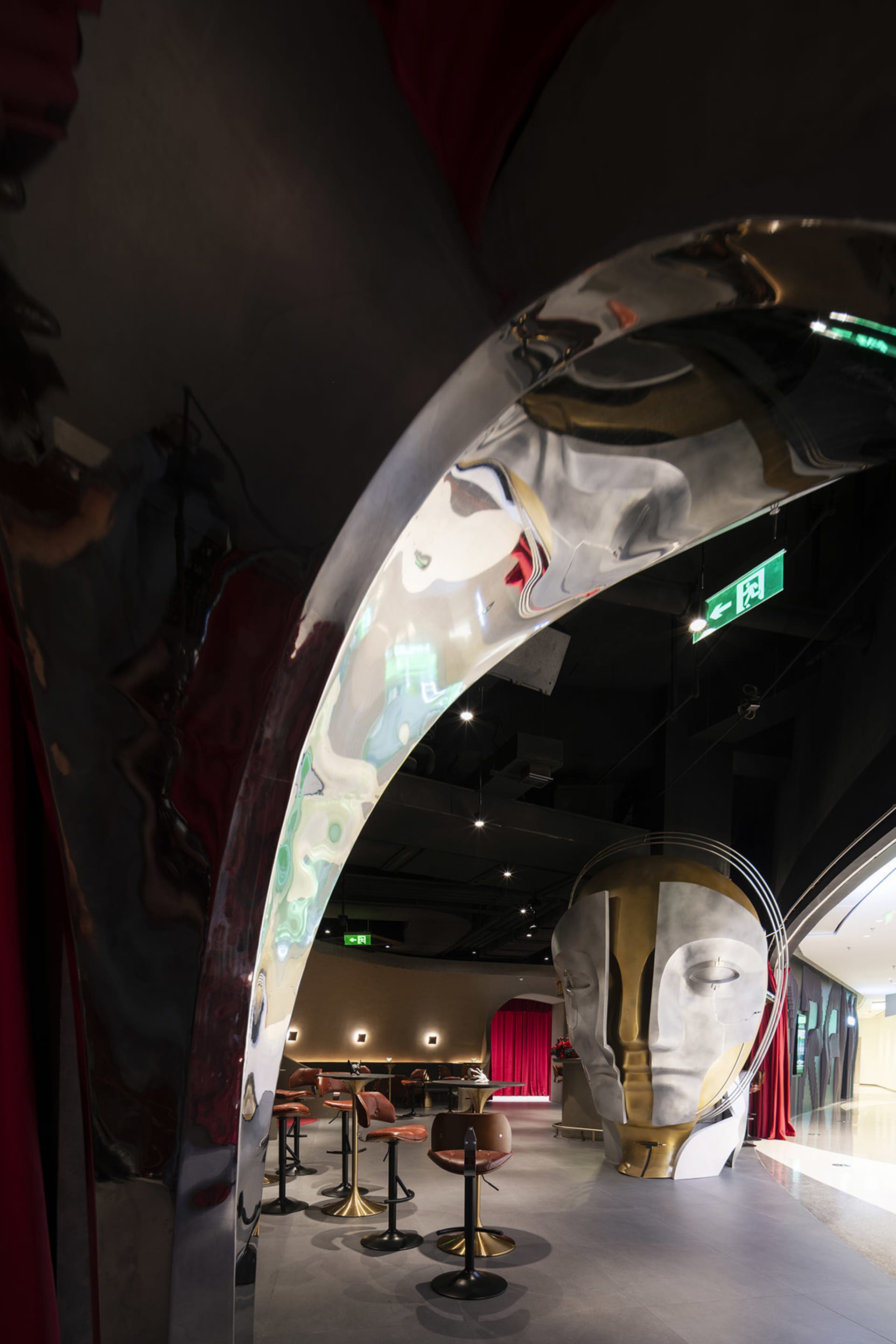 A room in a building featuring a large sculpture of a head surrounded by smaller sculptures, with a red curtain adding warmth to the space