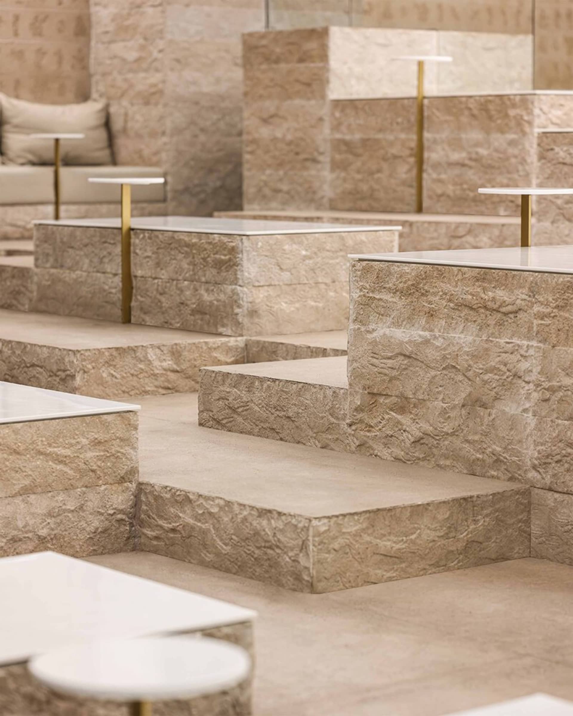 A modern and minimalistic indoor space with stone flooring, featuring steps leading to different levels and couches placed throughout