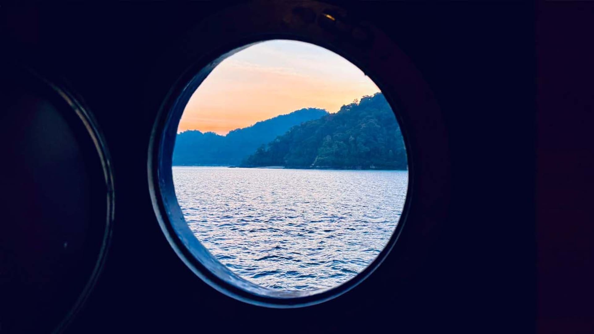 Calm ocean view through a round window on a boat, with the cabin visible in the background