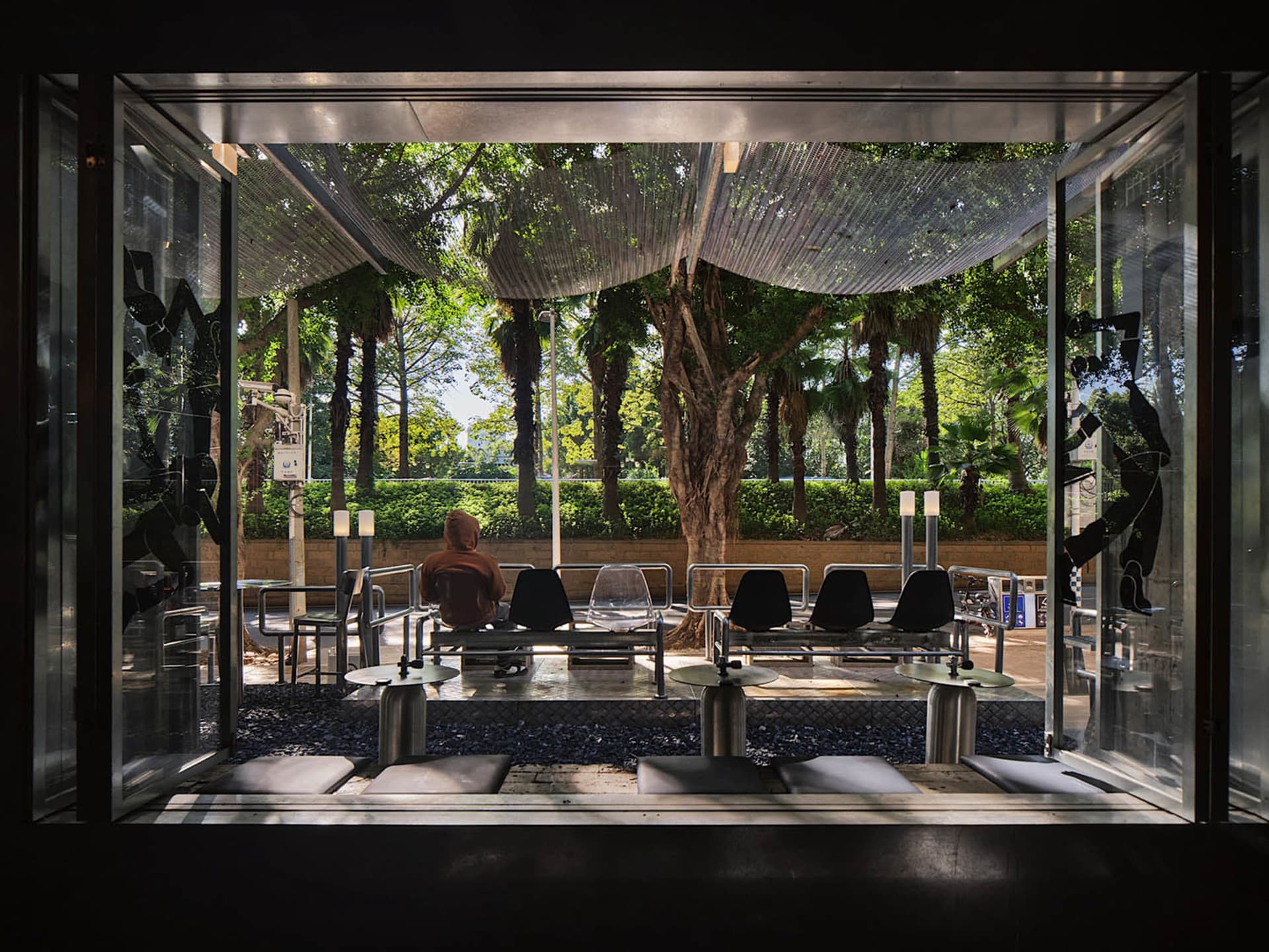 Outdoor seating area with various chairs and tables on a cement surface, surrounded by trees and natural light