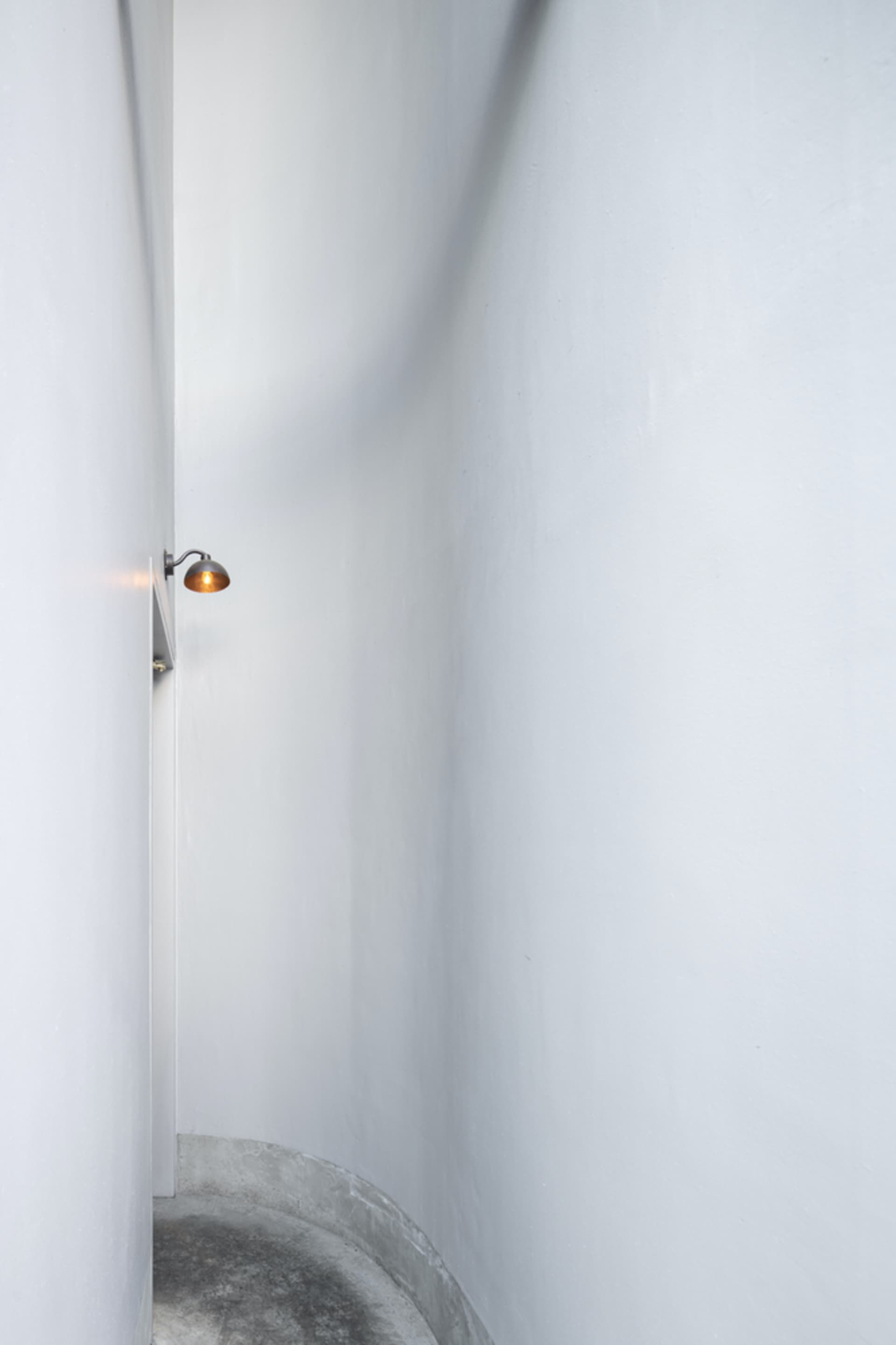 A minimalist white wall with two lights mounted on it, in a possibly empty hallway or small space