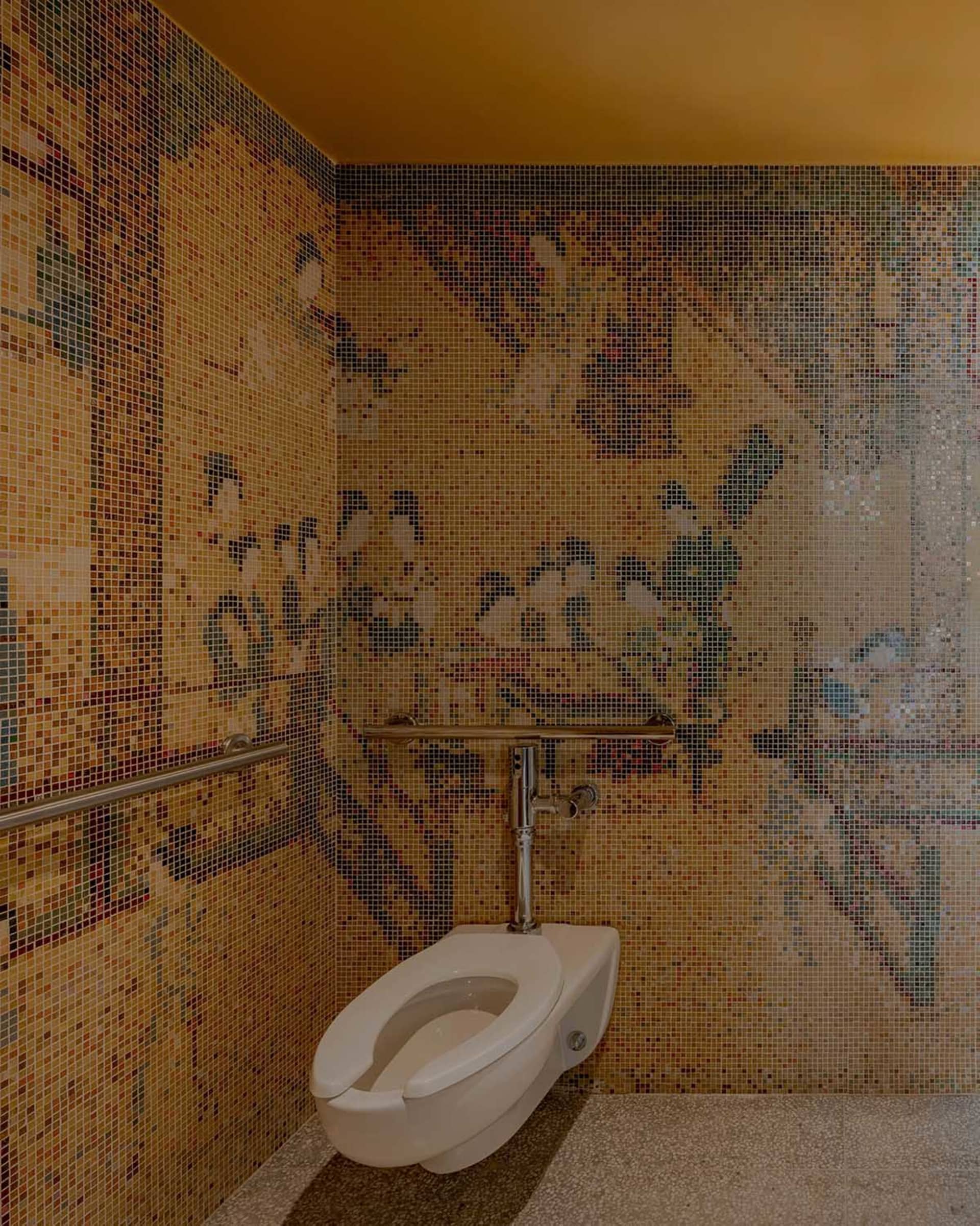 A modern bathroom with a white toilet in front of a yellow wall featuring an artistic design with people and other elements