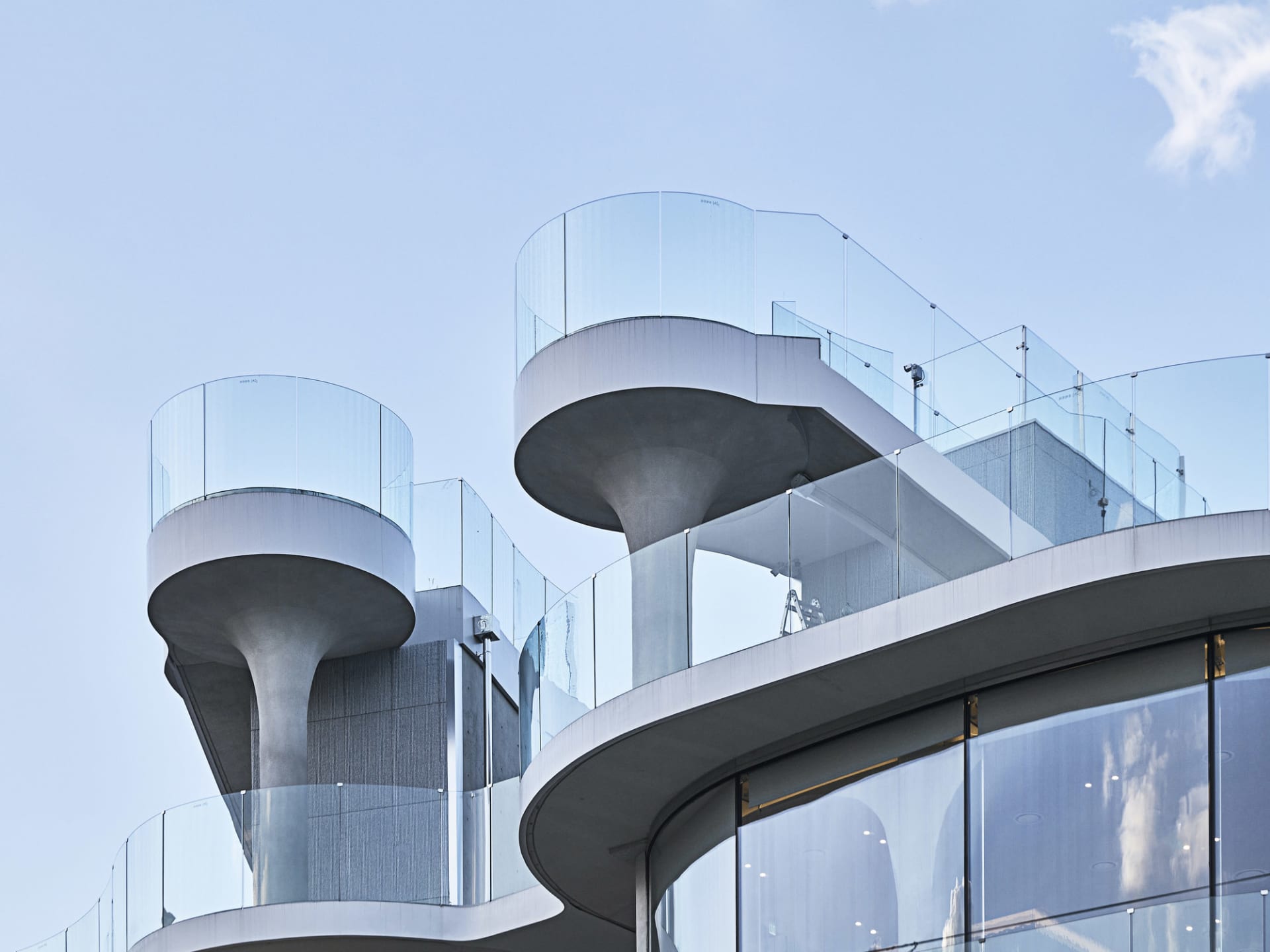 A modern building with a sleek glass facade and multiple levels, featuring a balcony and a focus on glass as a design element