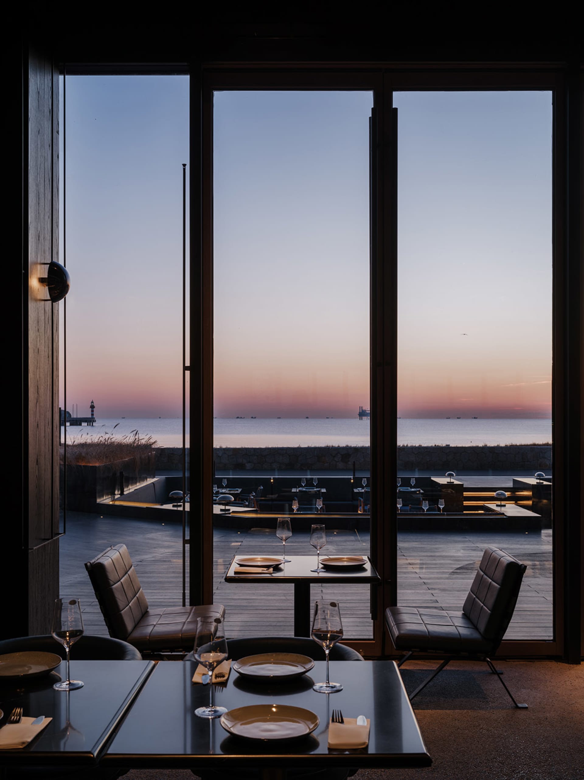 Modern restaurant interior with dining area, tables, chairs, and large windows offering an ocean view, well-lit and inviting