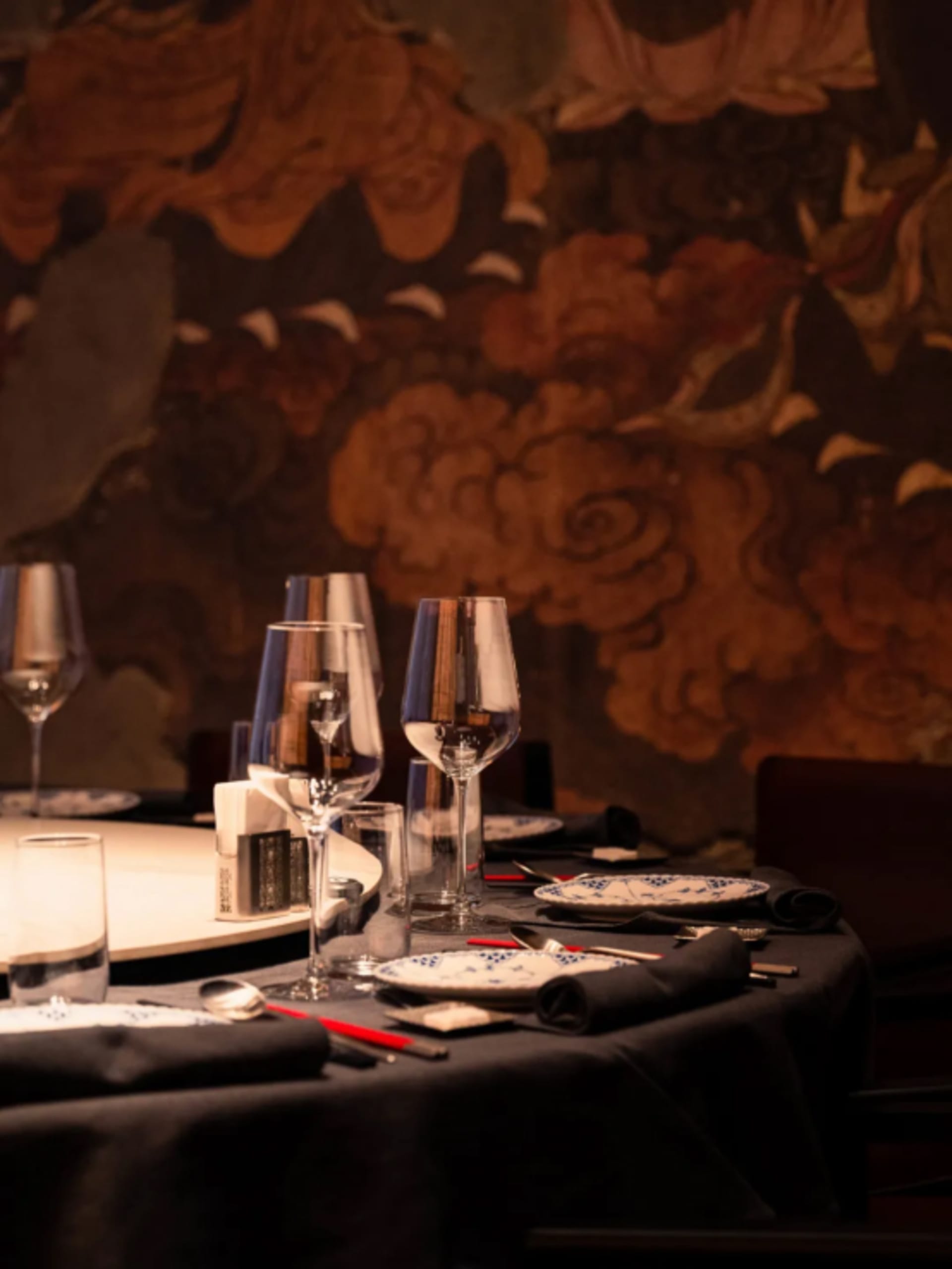Elegant dining area with a round table set for a formal dinner, featuring white plates, glasses, and wine glasses, in a sophisticated setting