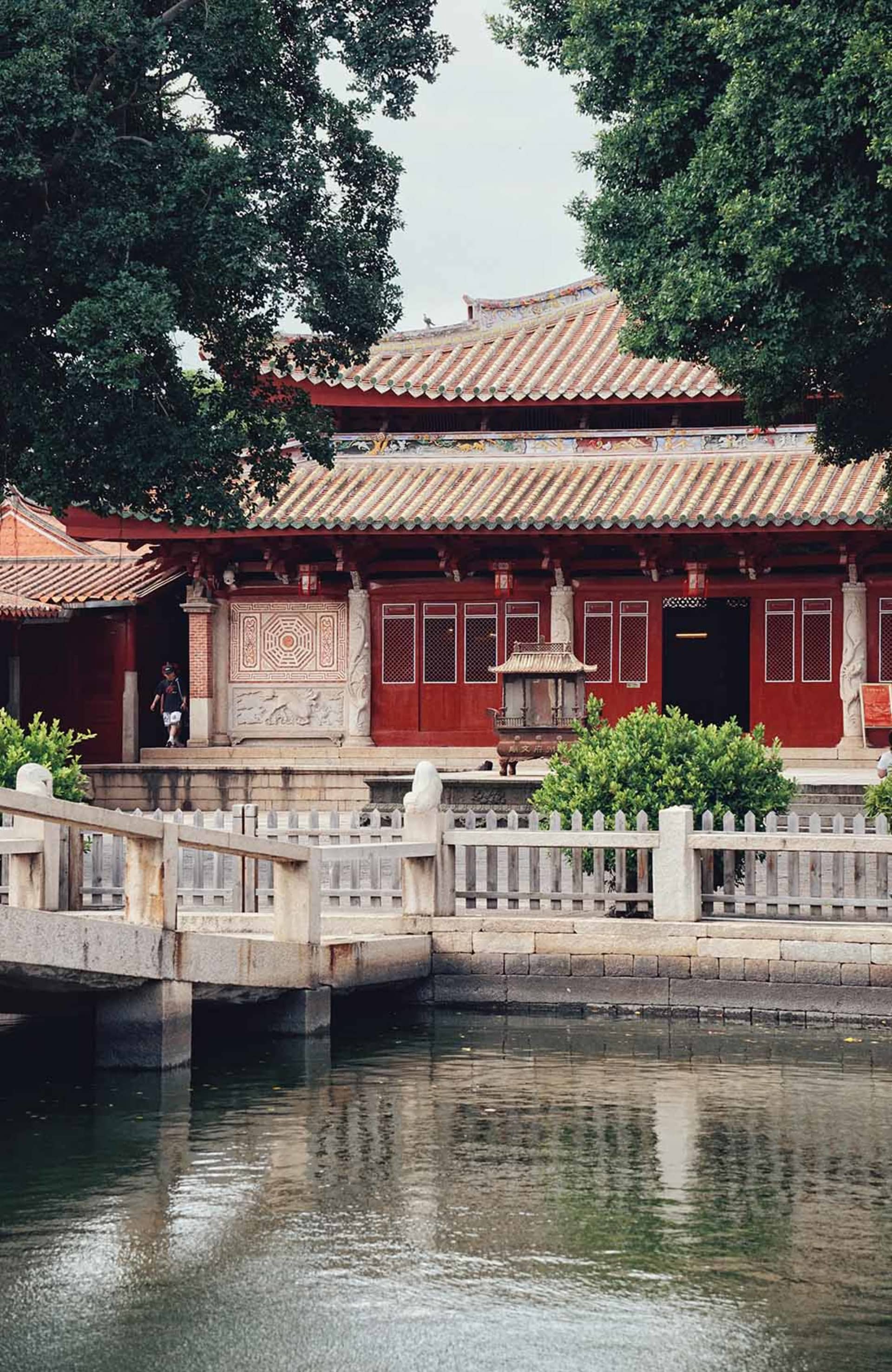 一座寧靜的亞洲風建築，擁有紅牆與白色線條，周圍環繞中庭與多個房間，人們在周邊走動
