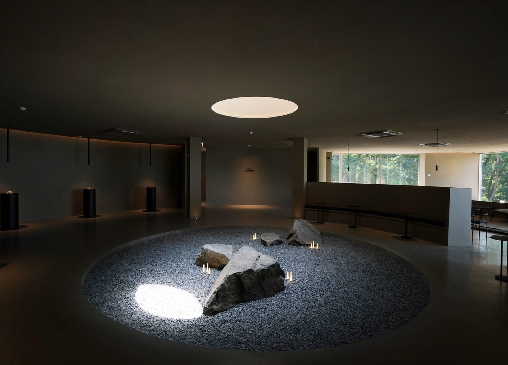 A serene indoor space with a large rock surrounded by smaller rocks and two benches, creating a calm atmosphere