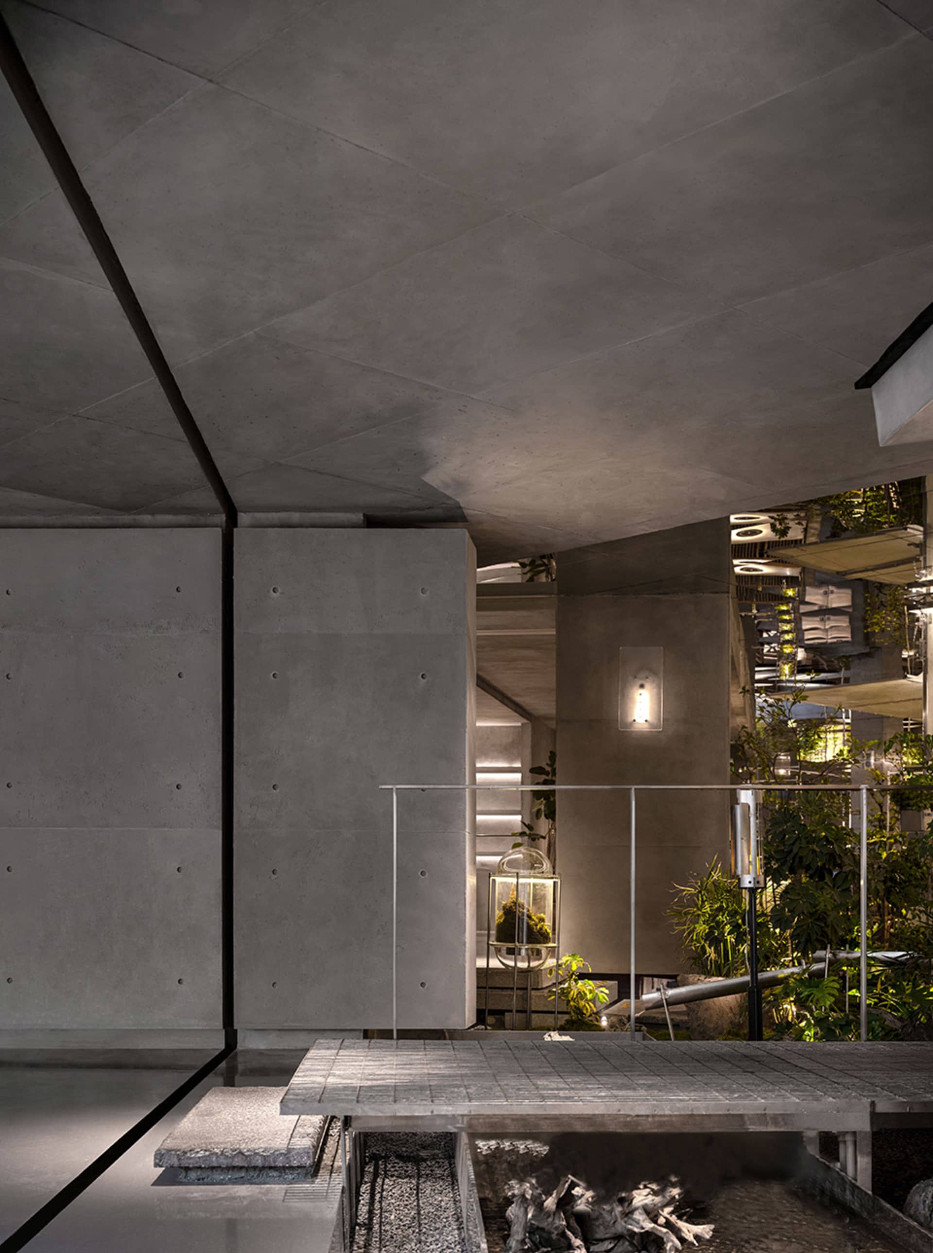 Modern building with a large glass wall, potted plants, and a mix of concrete and metal elements, emphasizing openness and natural light