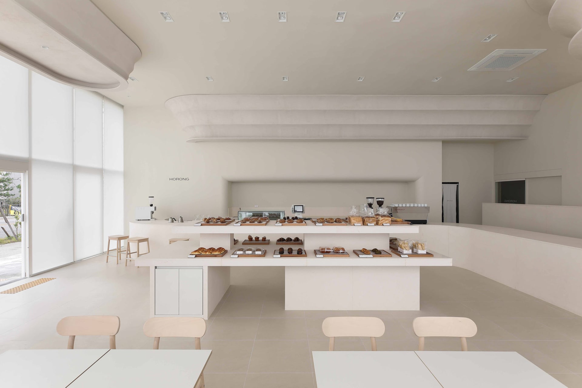 A modern cafe with white walls, a large counter displaying pastries and desserts, and multiple chairs in the dining area