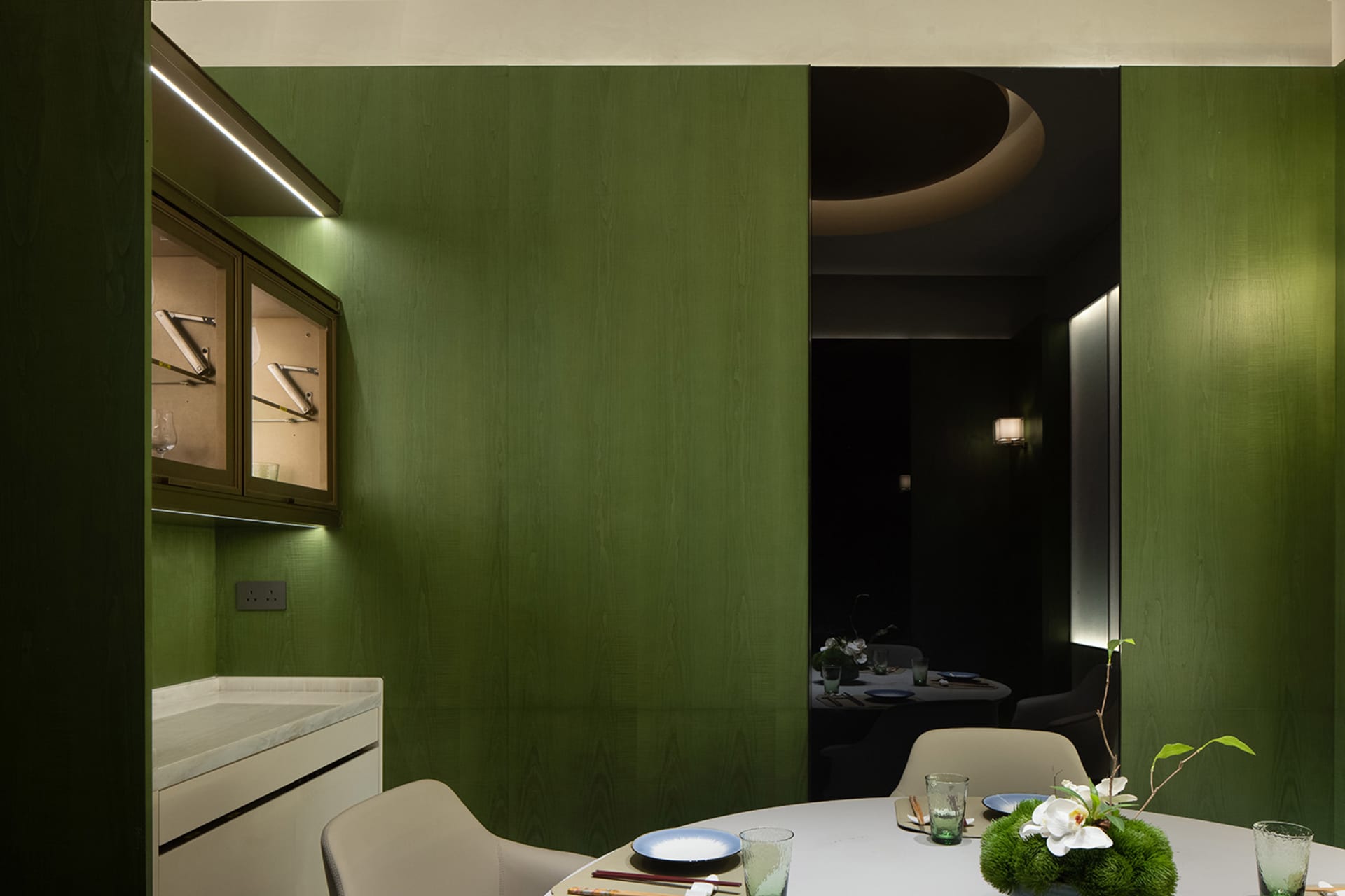 A modern kitchen and dining area with green walls, a dining table, chairs, and various decorative items