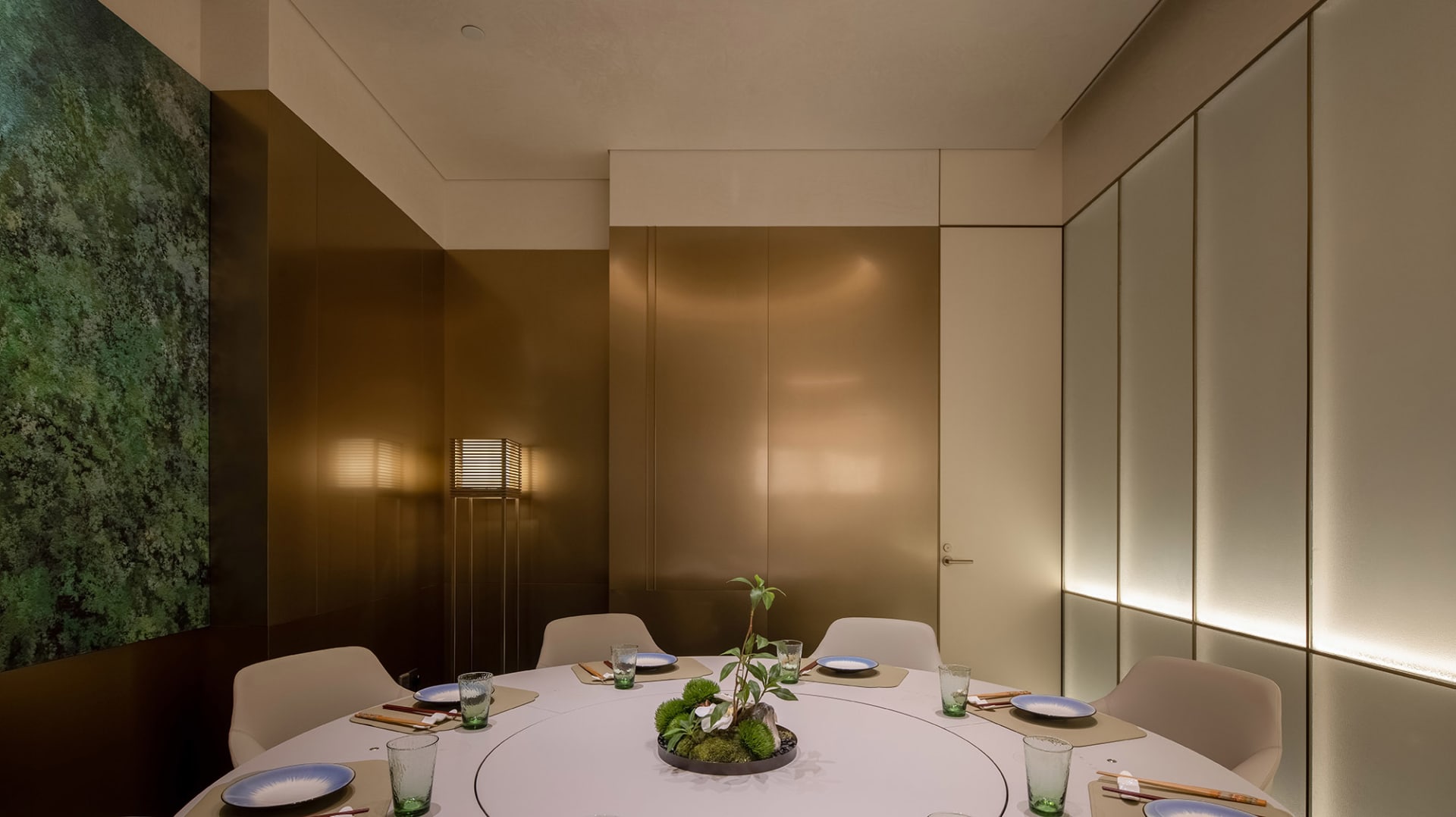 A formal dining area with a round table set for a dinner event, surrounded by chairs and decorated with various items