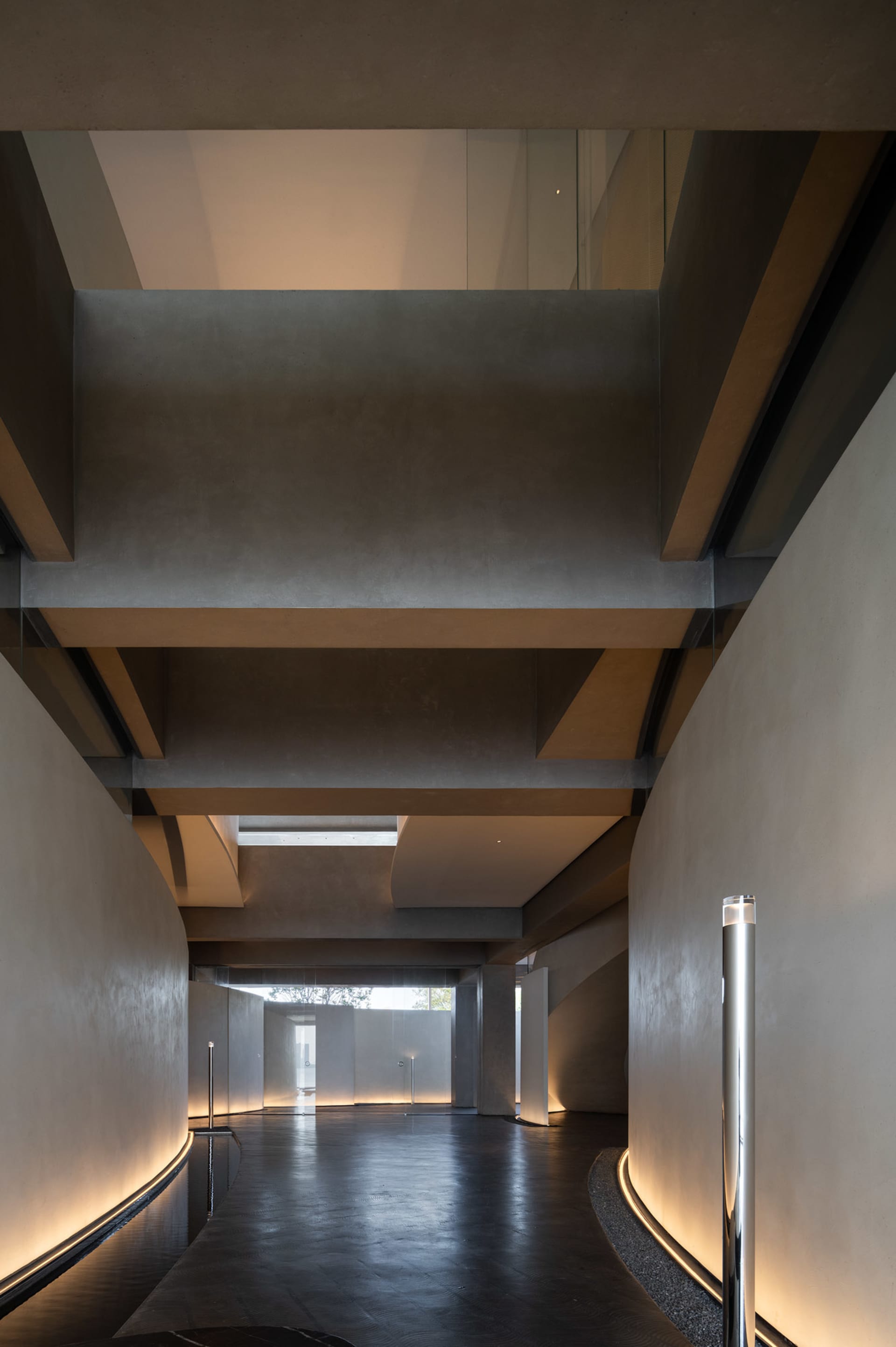 Industrial-style hallway with concrete walls, a staircase, and natural light from a small window, illuminated by two lights