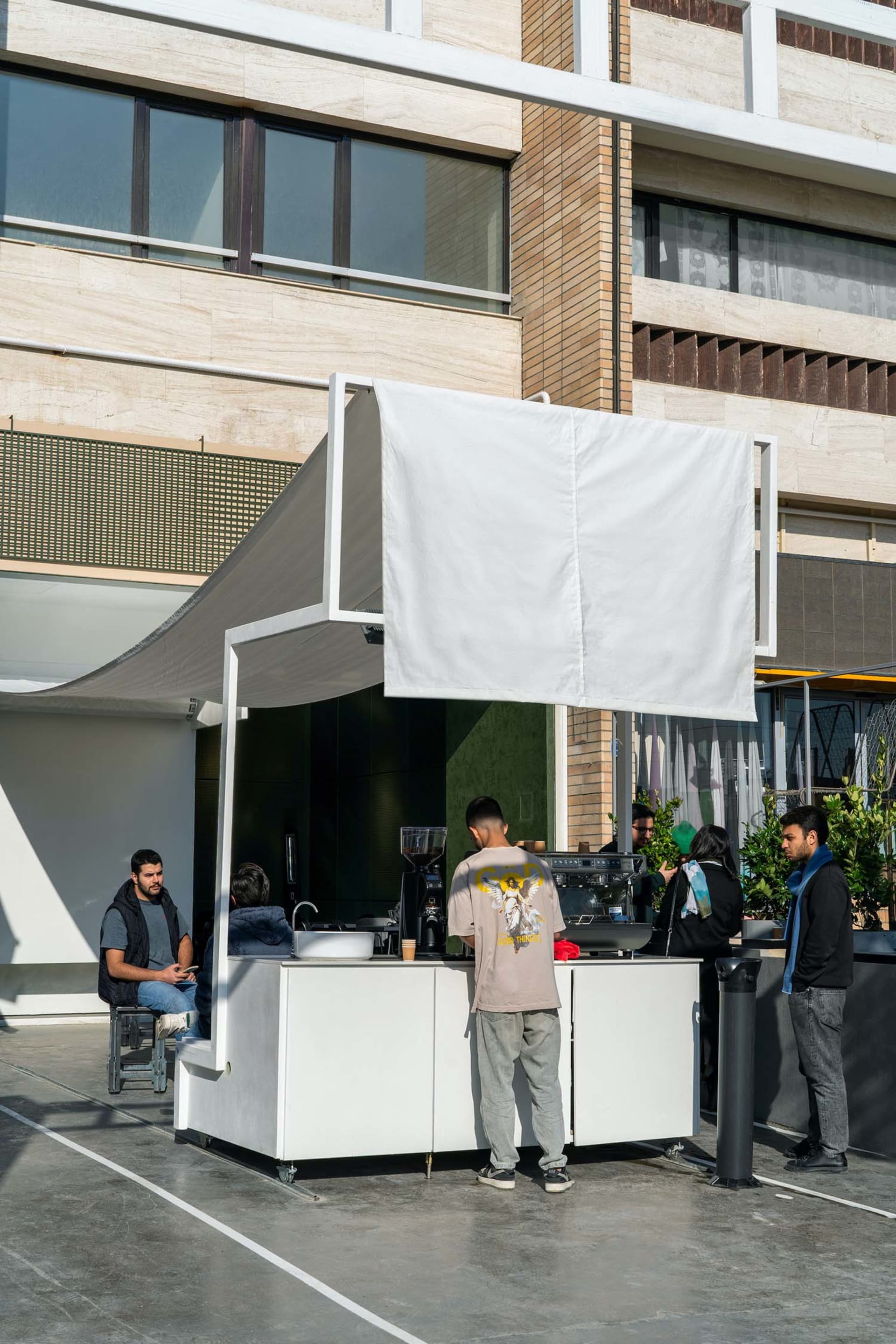 An outdoor cafe with white canopies, tables, and chairs, featuring a casual atmosphere and lively public space
